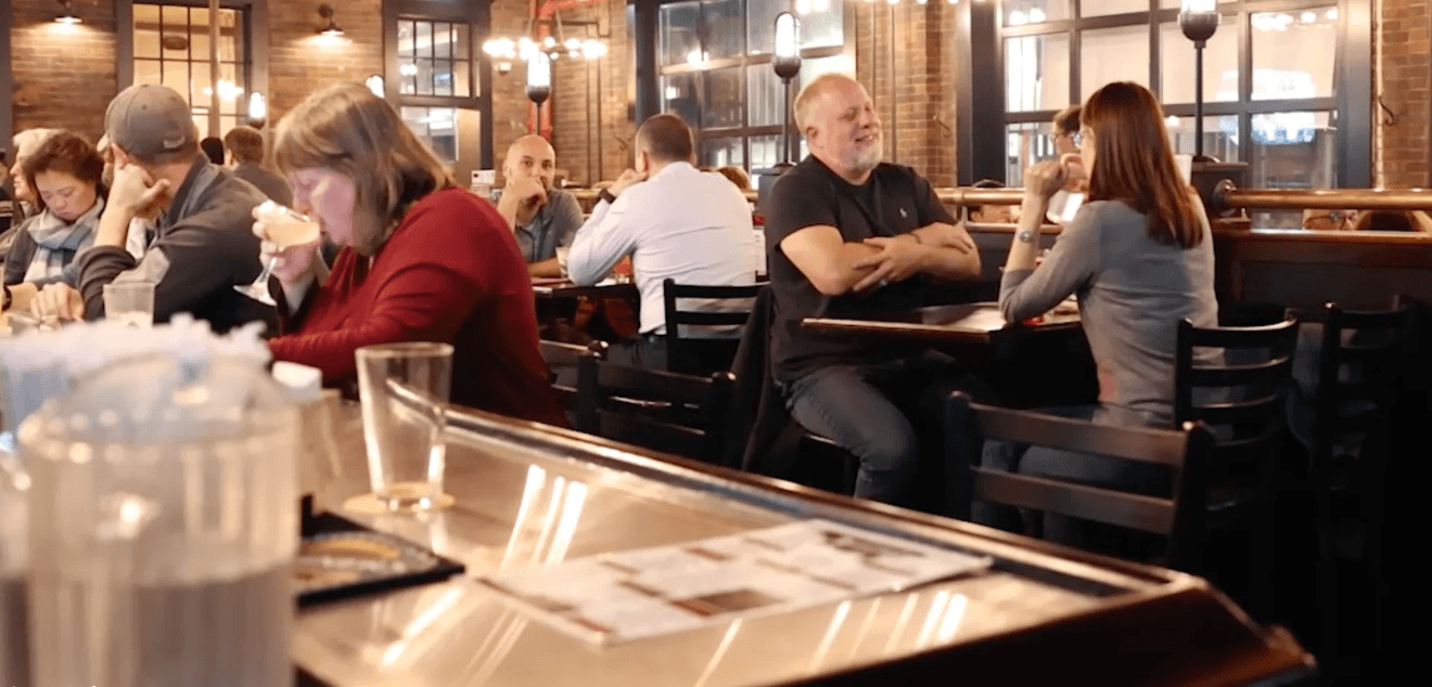Firehouse Grill's warm wood-paneled dining room, a lit neon sign over the doorway and a crowd mingling near the bar