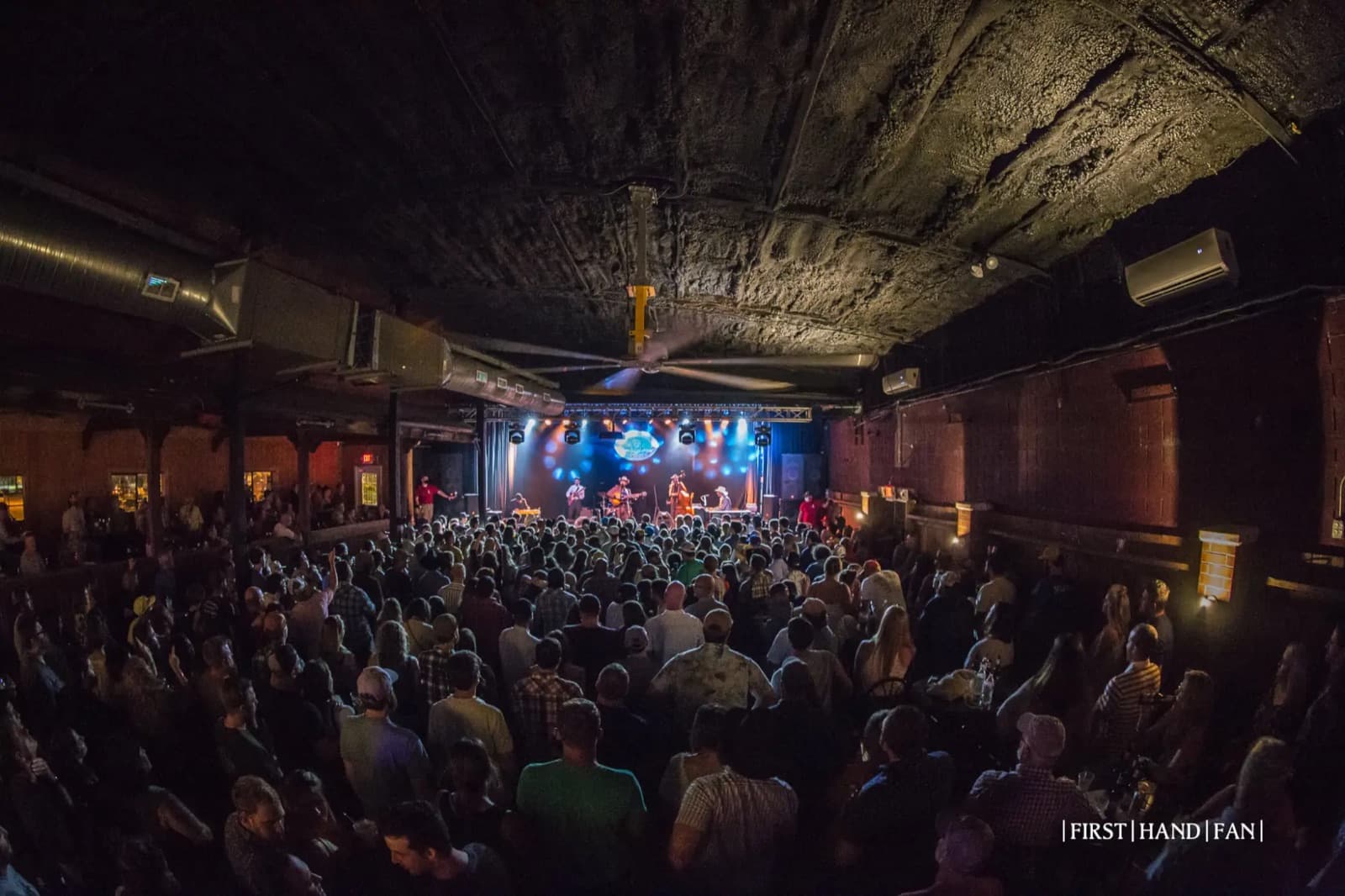 A band performing to a packed crowd at George's Majestic Lounge, lit in blue and green stage light