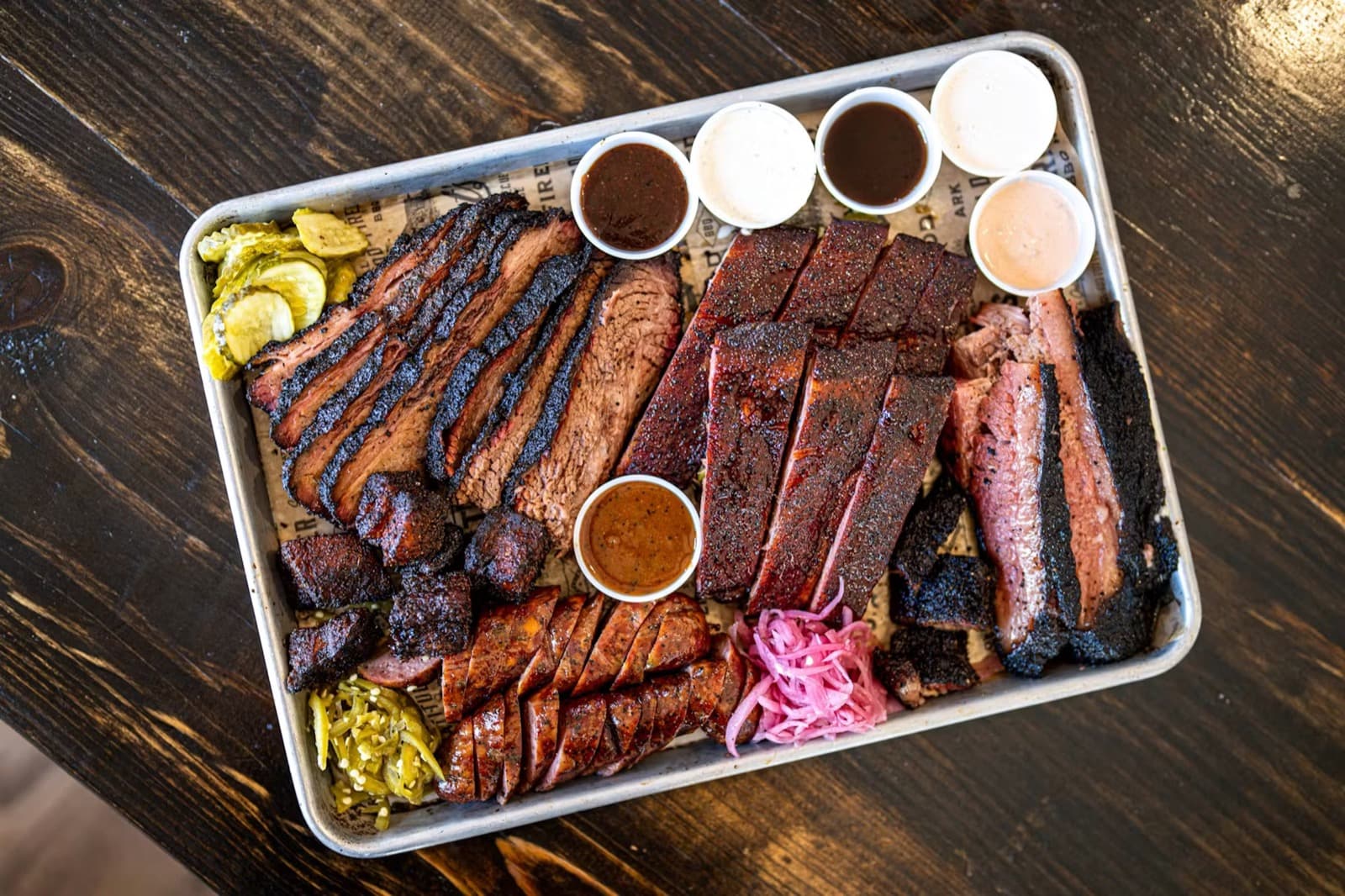 A sliced smoked BBQ tray at Wright's Barbecue with sauces, pickles, and red onions
