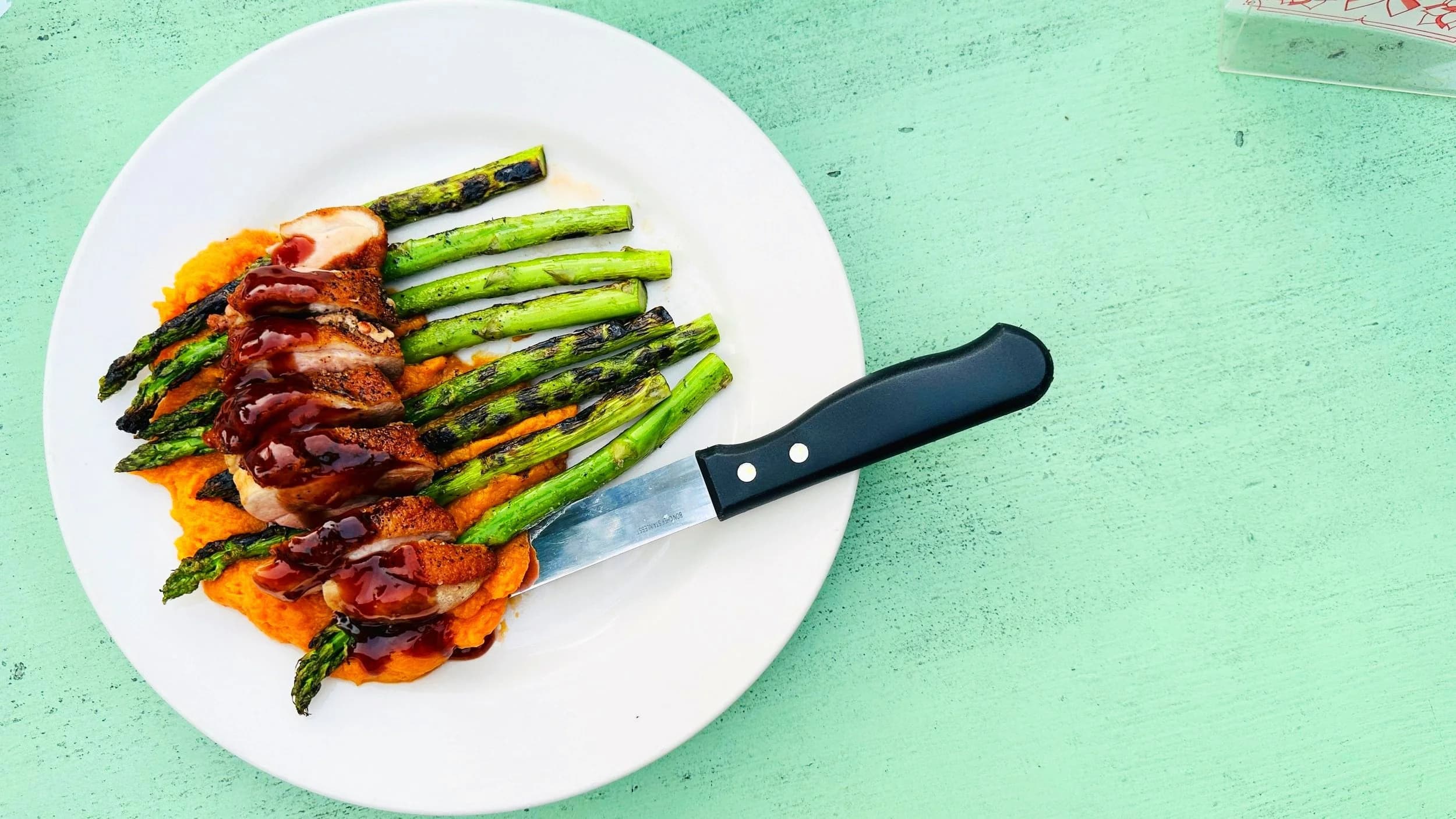 An overhead shot of a sliced pan-seared duck breast glazed in berry sauce over sweet potato mash with grilled asparagus at The TOP