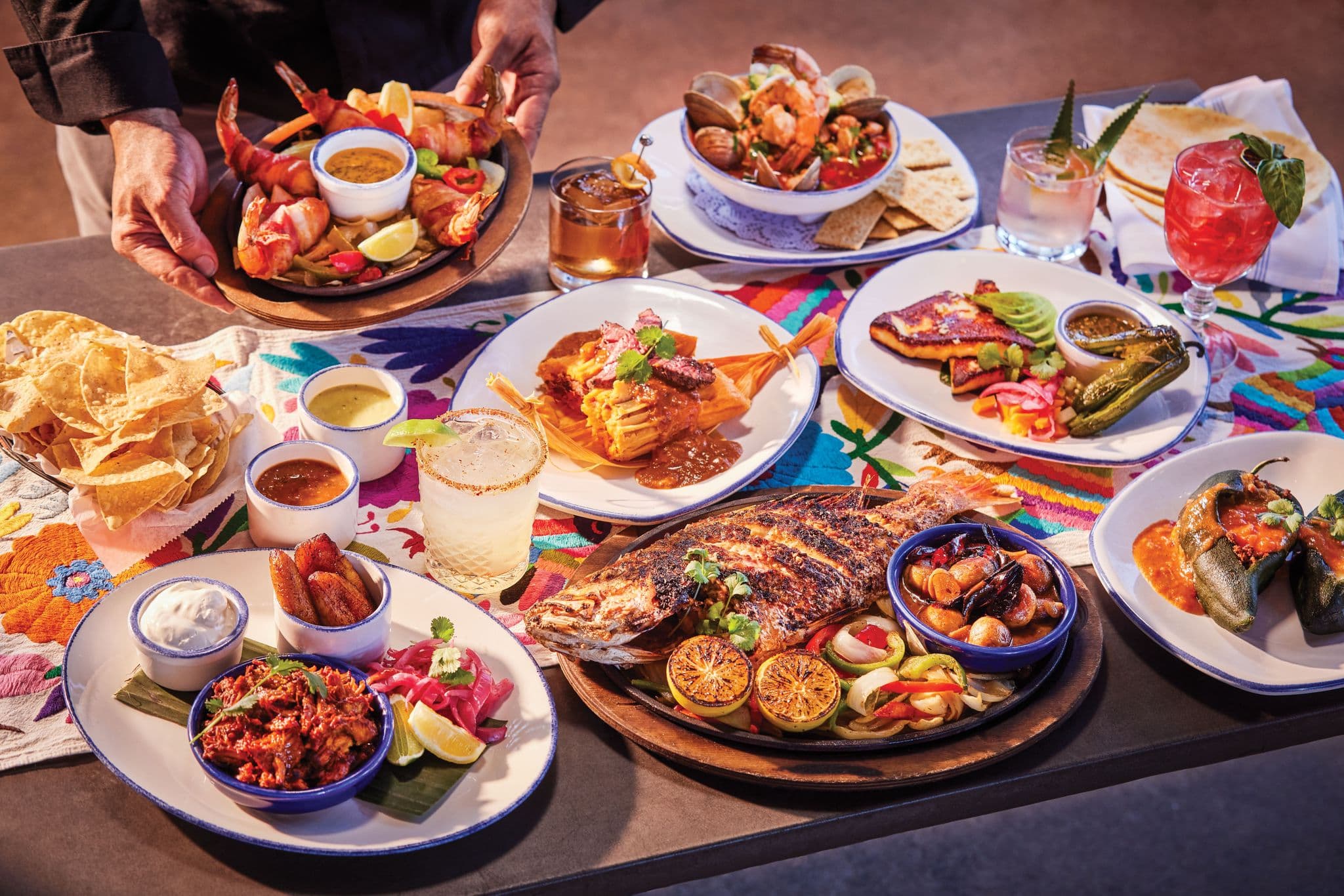 A loaded Ninfa's tableside spread — grilled seafood, a whole grilled fish, enchiladas, stuffed poblanos, tacos, chips, and margaritas