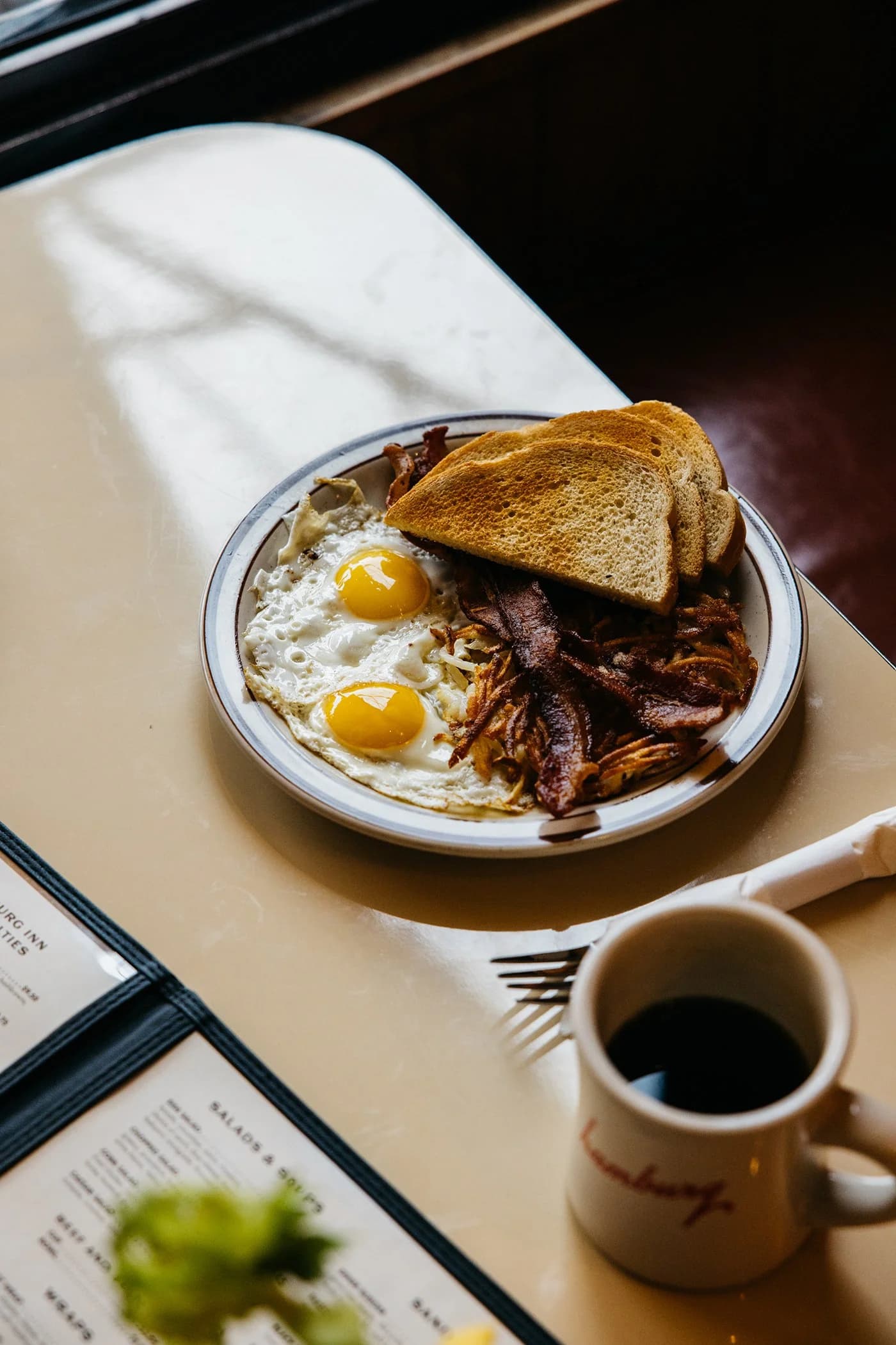 An overhead shot of a breakfast plate at Hamburg Inn No. 2 — two fried eggs, hash browns, bacon, and toast, with a mug of coffee