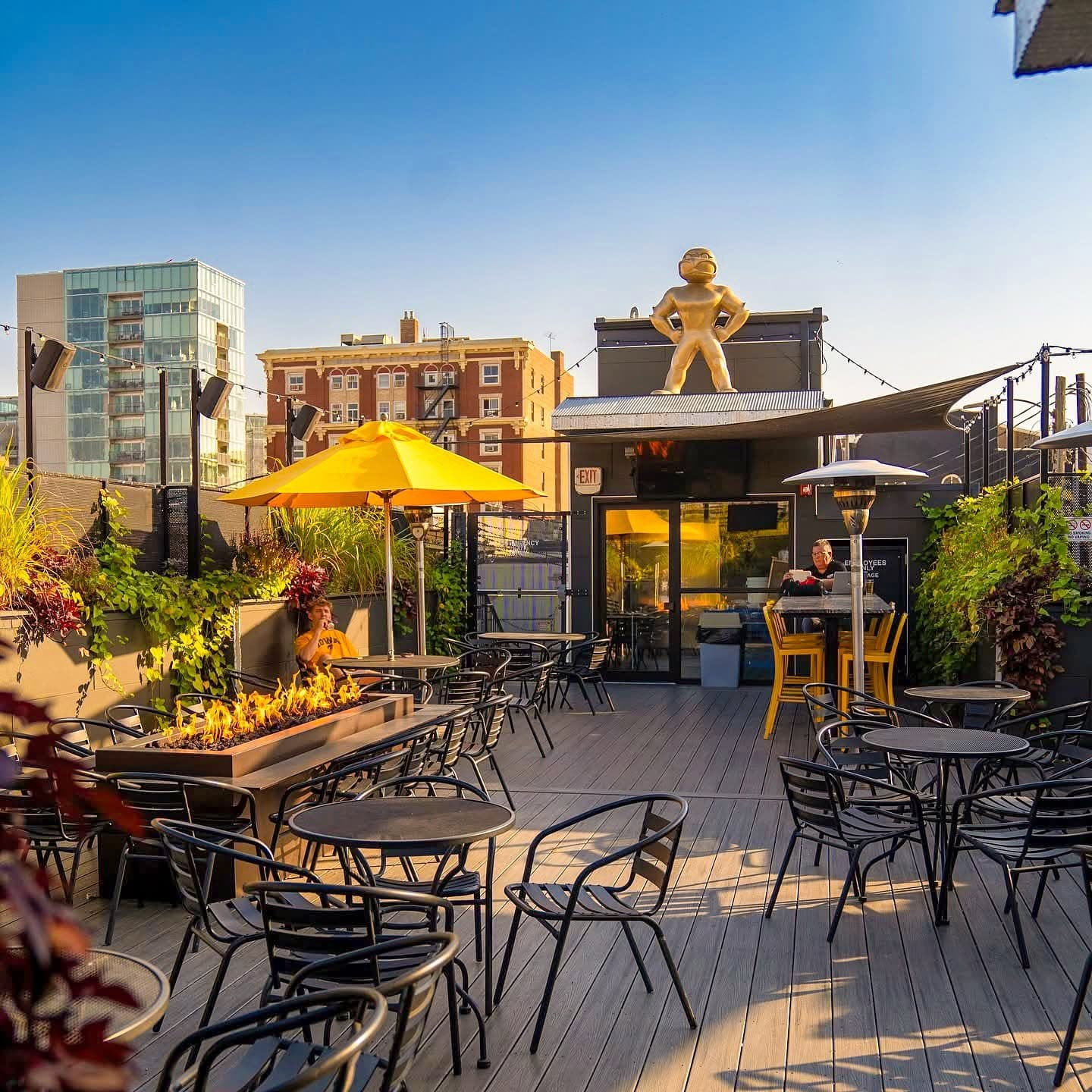 Joe's Place rooftop patio at golden hour with a fire pit, string lights, and a giant gold Herky the Hawk statue on the roofline