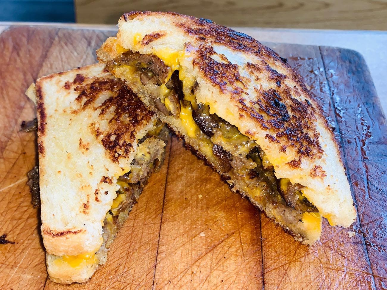 A steak and cheddar grilled cheese sandwich cut in half, showing the melted filling, on a cutting board at Marco's Grilled Cheese