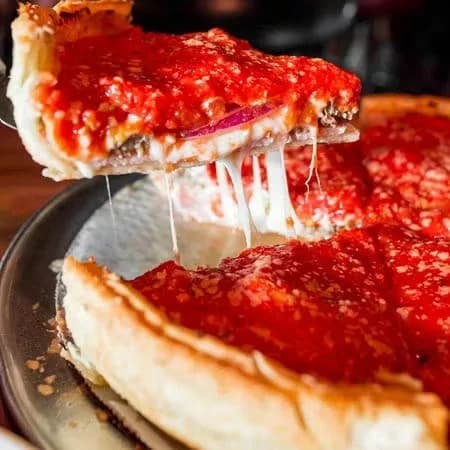 A cheesy slice of deep-dish pizza with red sauce being pulled up from the pie, strings of mozzarella stretching
