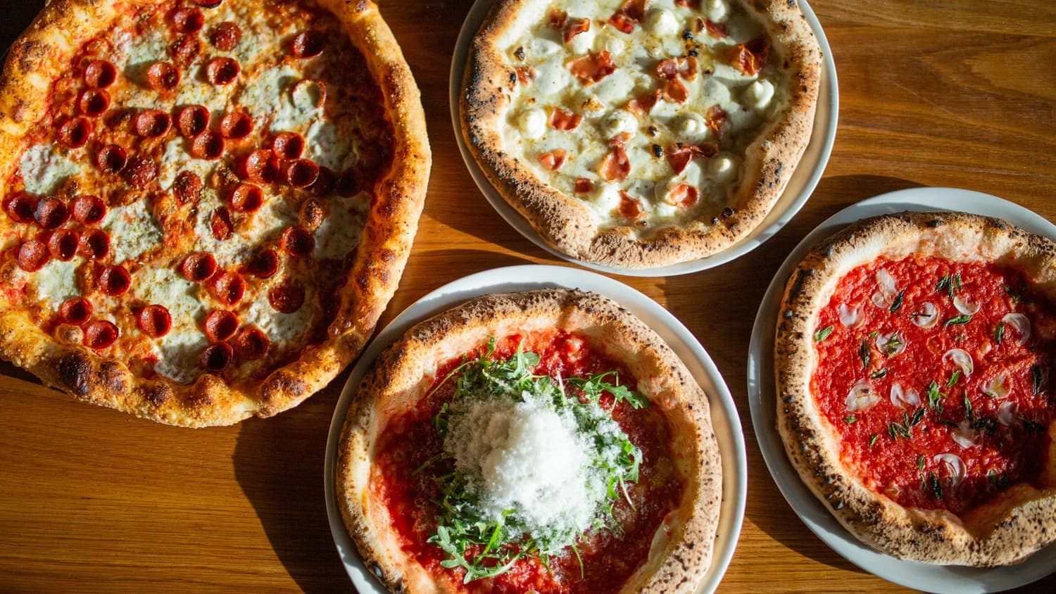 Four sourdough pies from A Dopo on a wooden table — pepperoni, prosciutto and mozzarella, and two Margherita-style pies