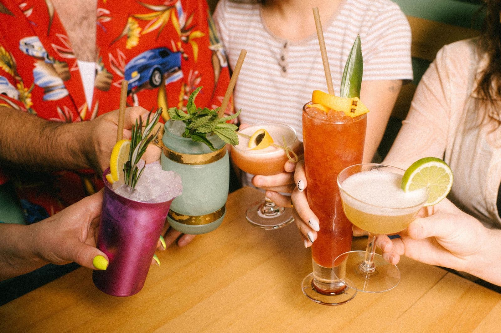 Three garnished tiki cocktails held up together at Tern Club — a purple frozen drink, a mug with mint, and a tall rum punch