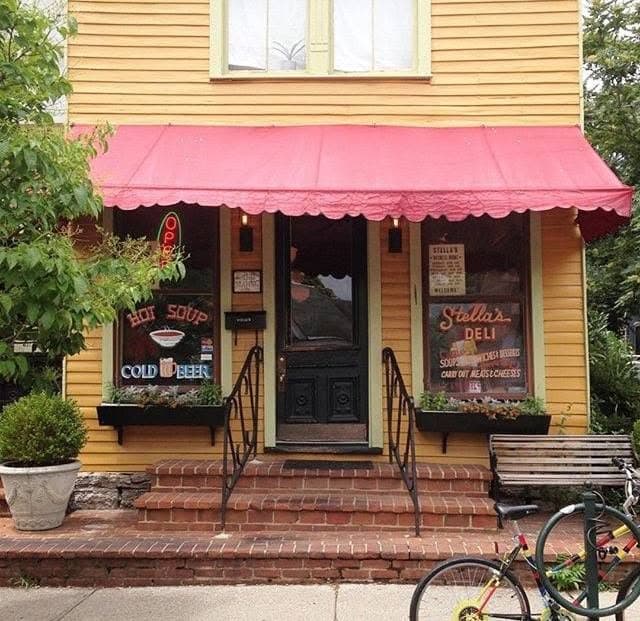 Stella's Kentucky Deli's yellow storefront with a red awning, neon 'Hot Soup Cold Beer' sign, and window boxes