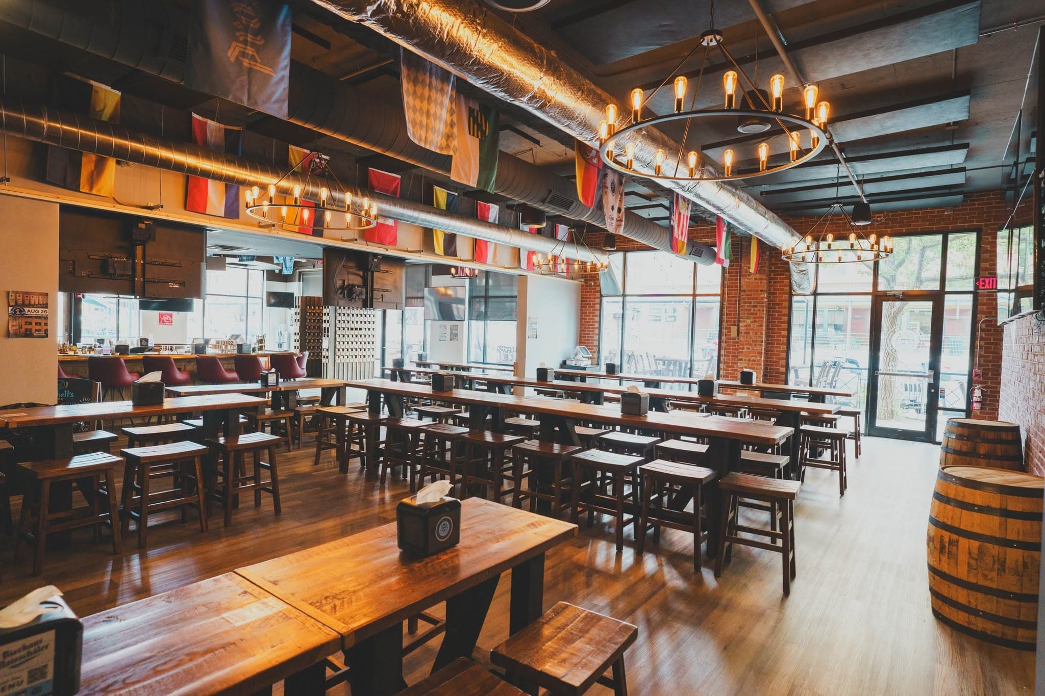 The interior of Bierhaus Maisschäler with long communal wood tables, ring chandeliers, and international flags hanging from the ductwork
