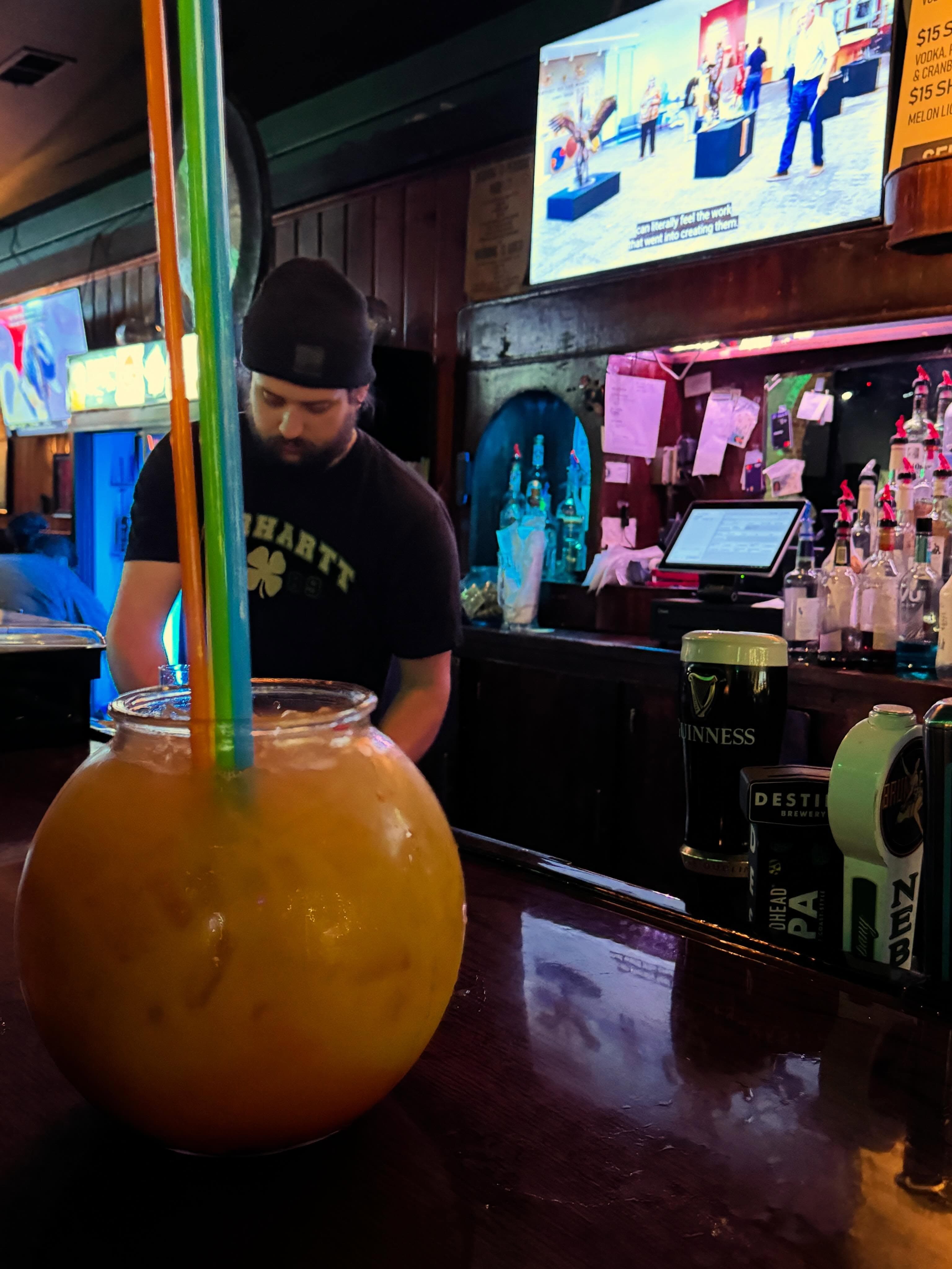A fishbowl cocktail with dual straws on Duffy's Tavern bar, the bartender and beer taps behind it