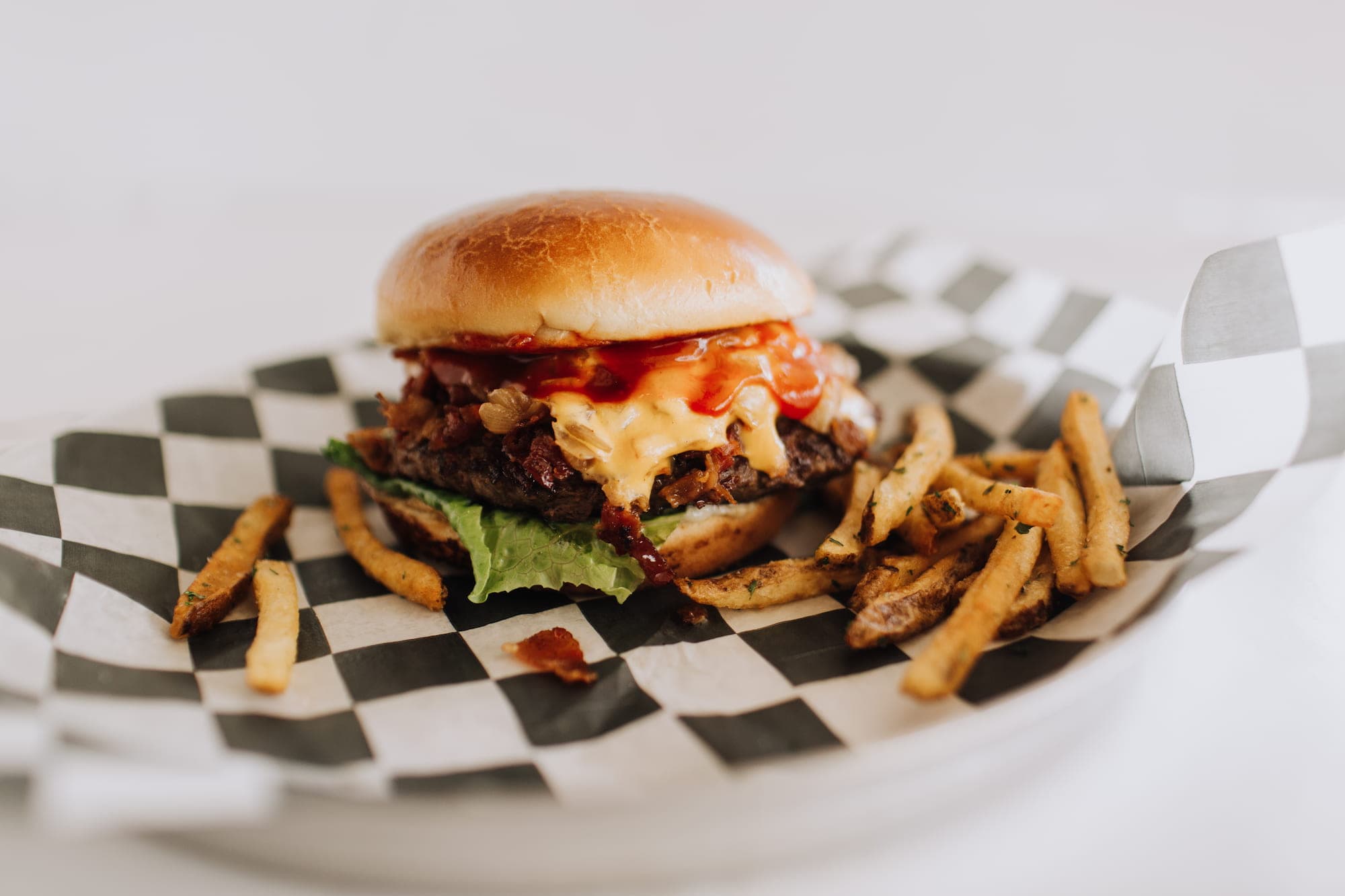 A bacon cheeseburger topped with barbecue sauce next to a pile of seasoned fries at Honest Abe's