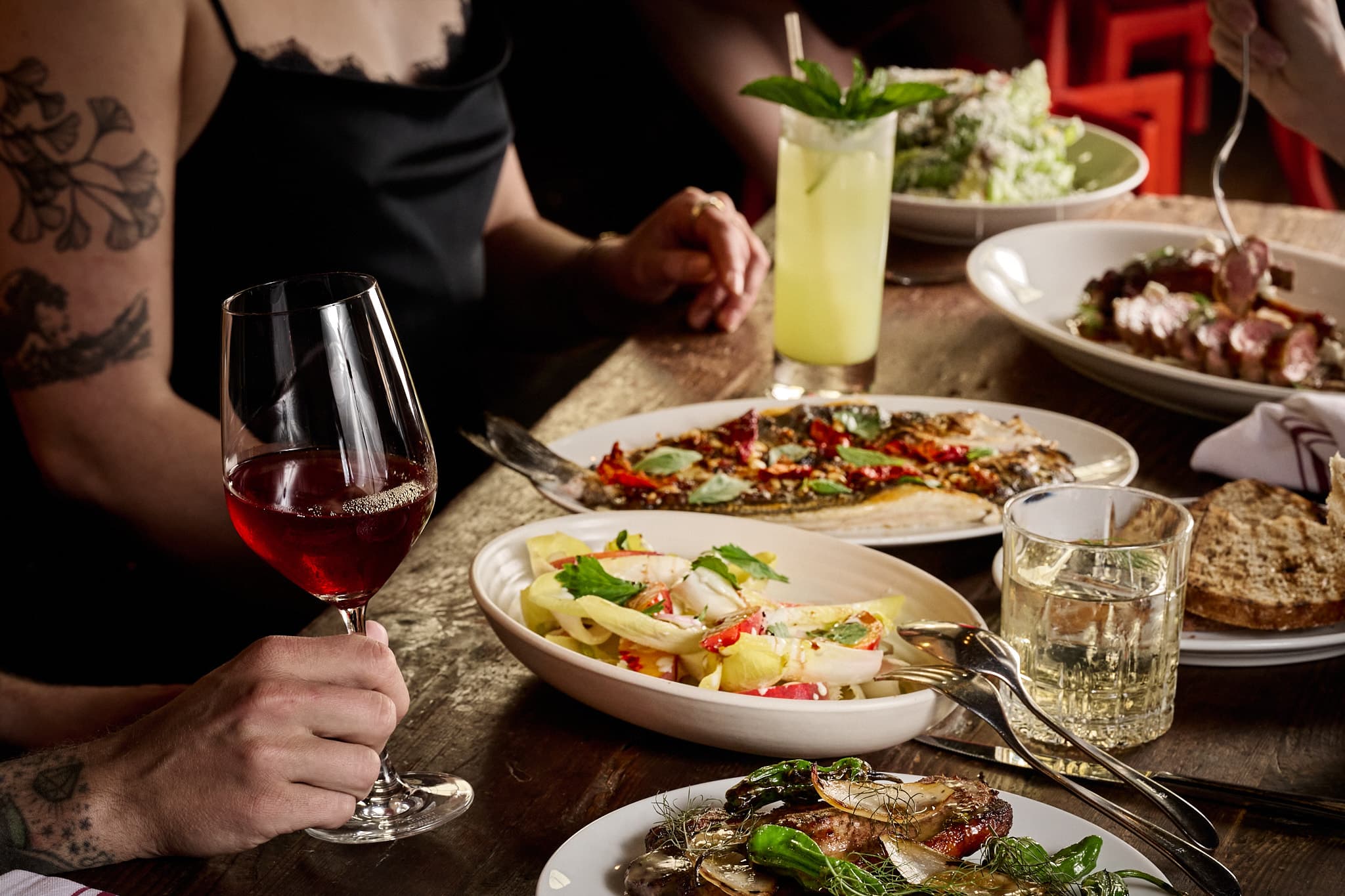 Table at Bestia loaded with shared plates — grilled whole fish, salad, charcuterie, and glasses of wine — on a rustic wood table
