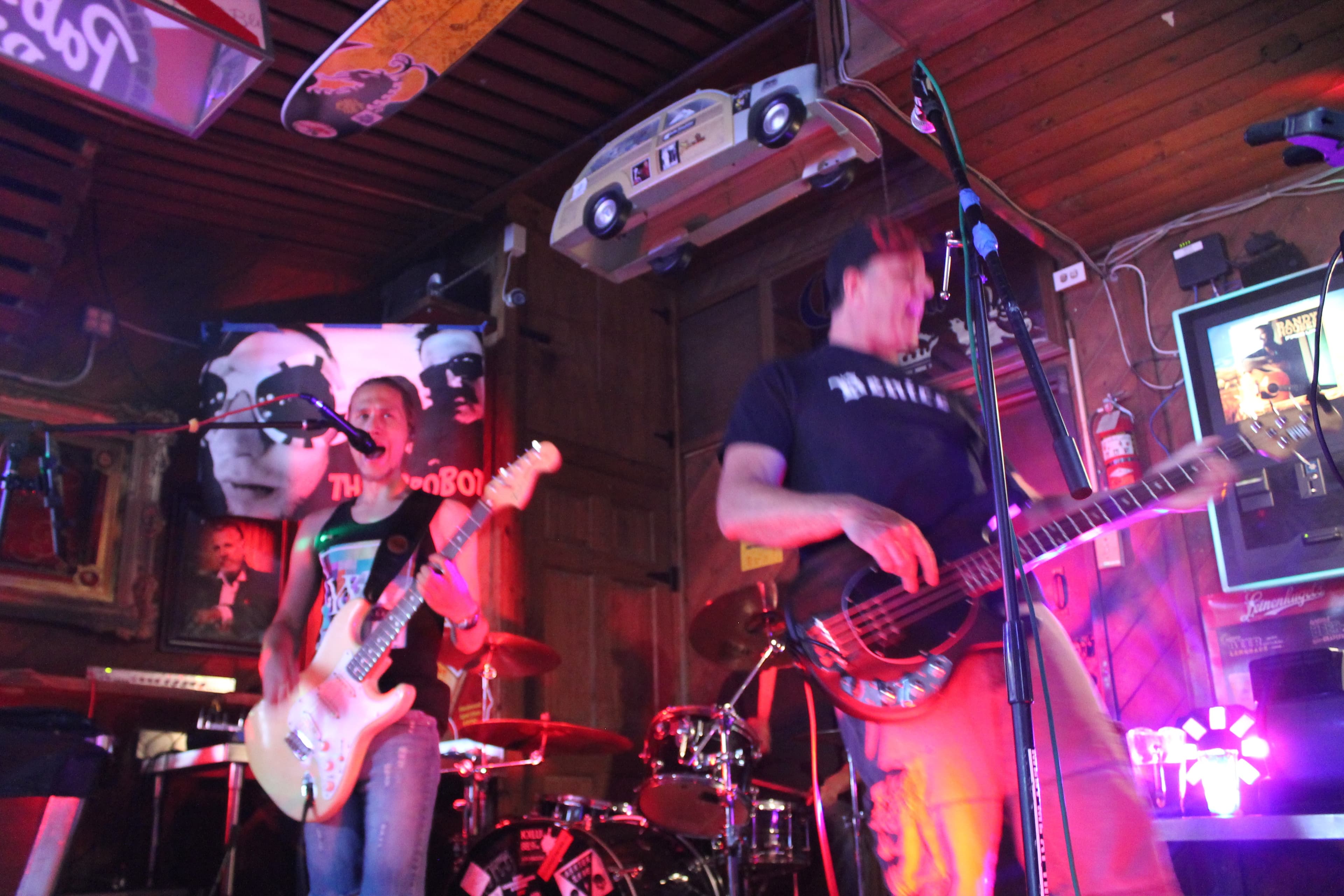 A band playing live inside Hinano Cafe's dive-bar interior, surfboards and band posters covering the wood-paneled walls