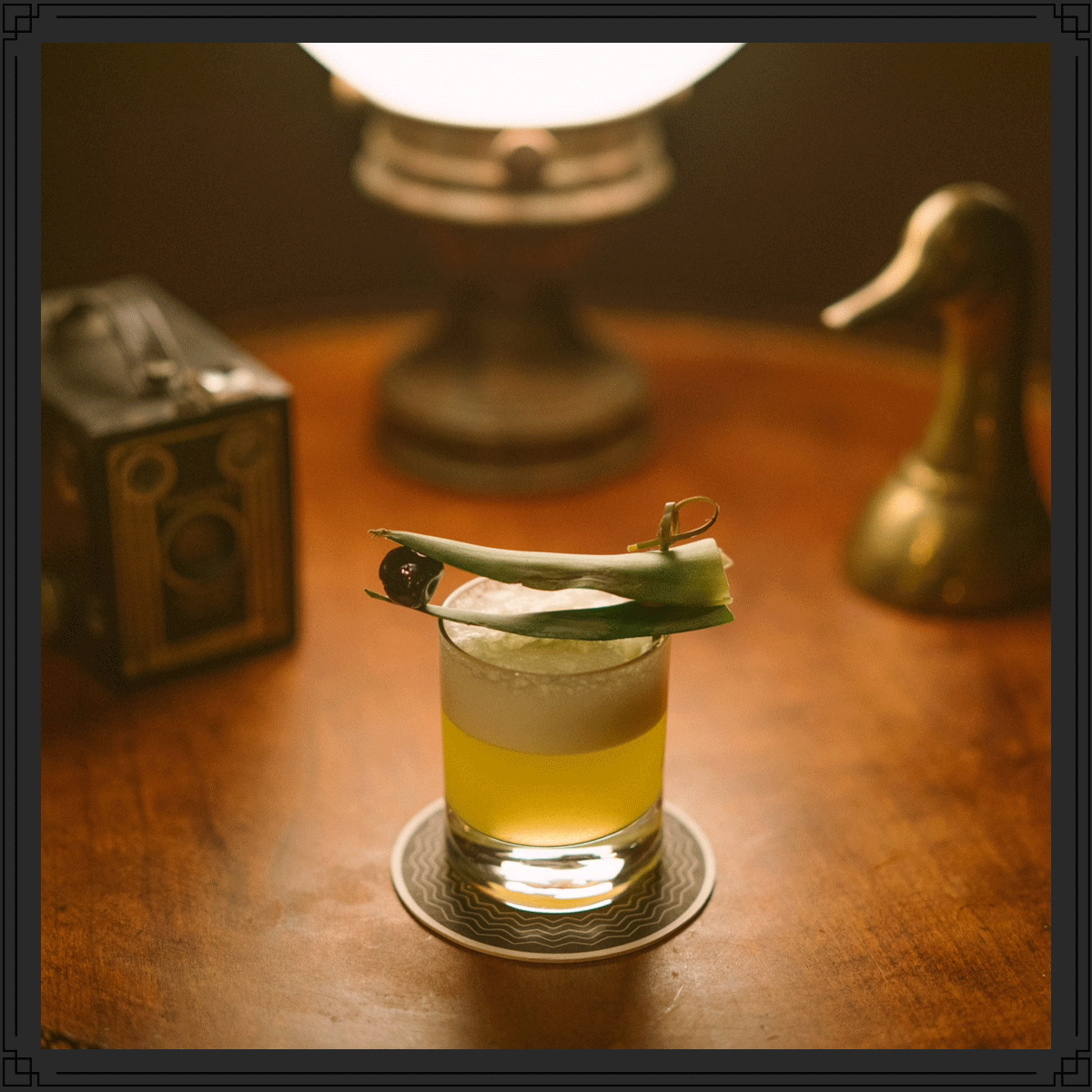 A garnished bourbon cocktail glowing on a candlelit wood table at Hell or High Water, vintage decor blurred behind it