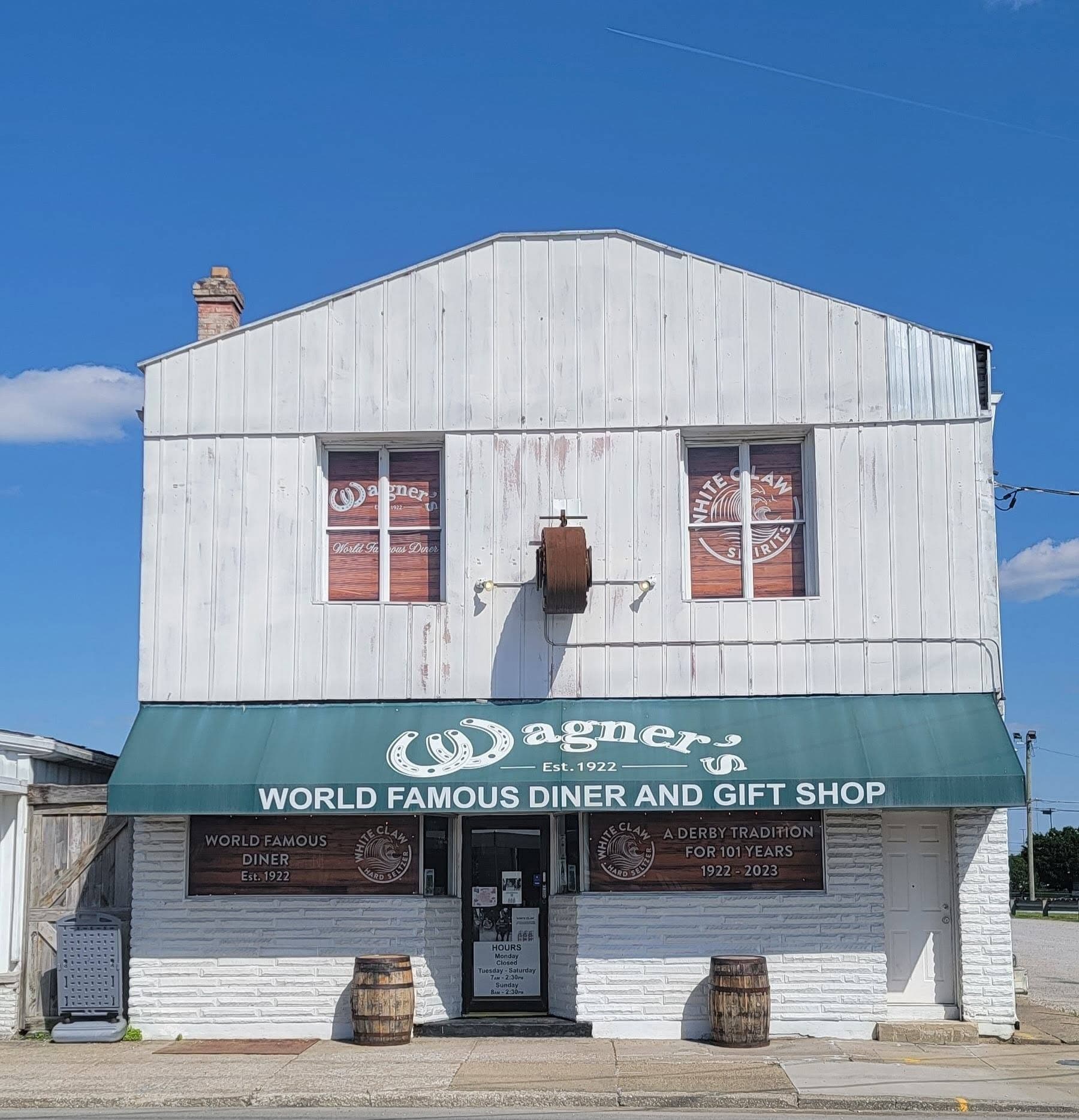 Wagner's Pharmacy's white metal-clad storefront with its green 'World Famous Diner and Gift Shop' awning and whiskey-barrel planters out front