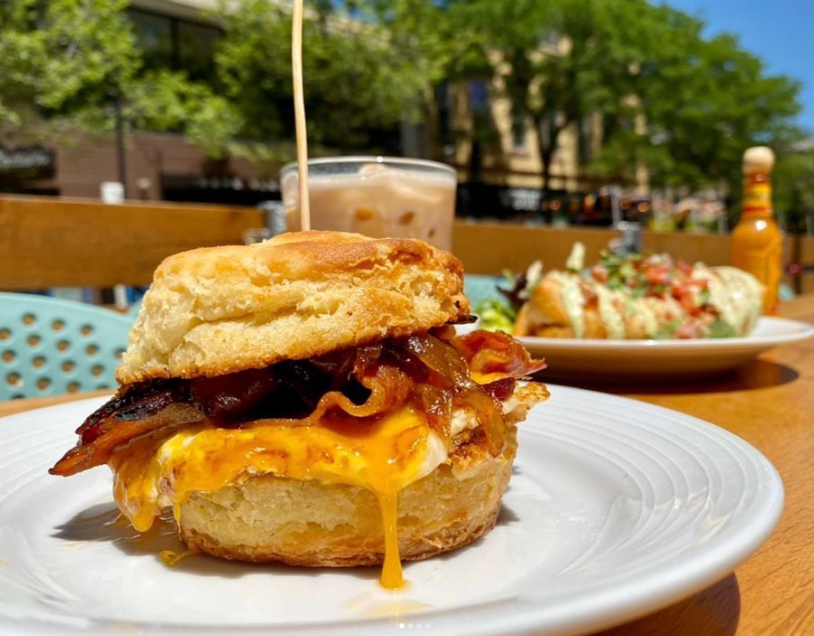 An overhead patio brunch spread at Ancora — a steak-and-eggs bowl, a glazed pastry, and cocktails