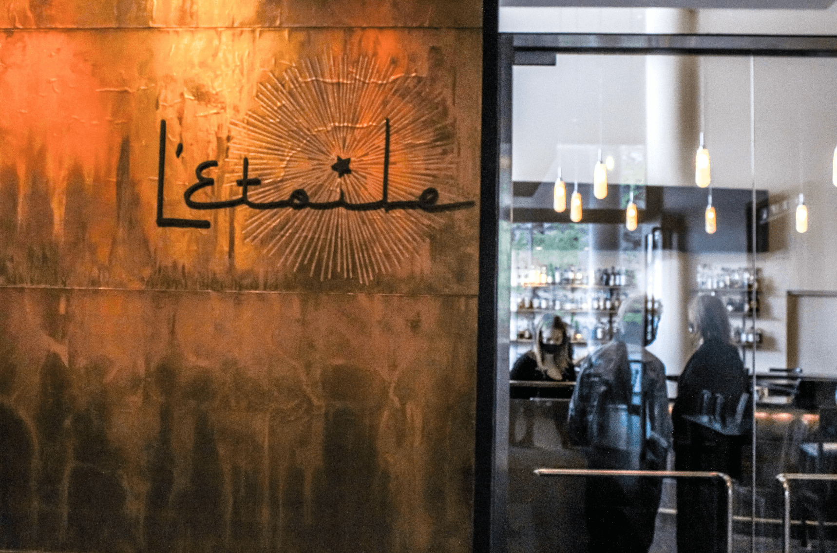 L'Etoile's storefront sign and sunburst logo on the building exterior, with the illuminated bar visible through the entrance