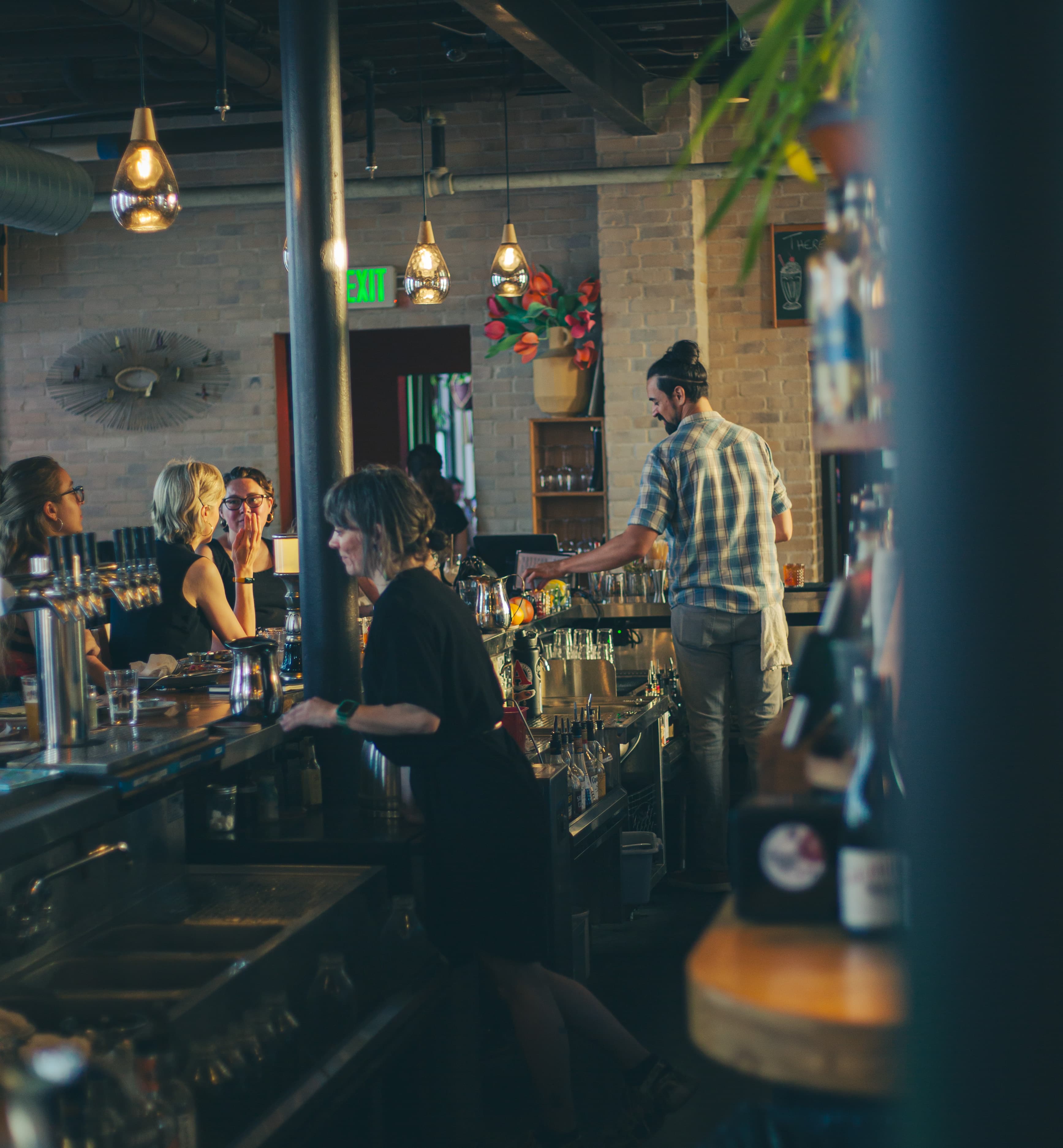Bartenders working behind the bar as guests chat at the taps, exposed brick and warm pendant lighting