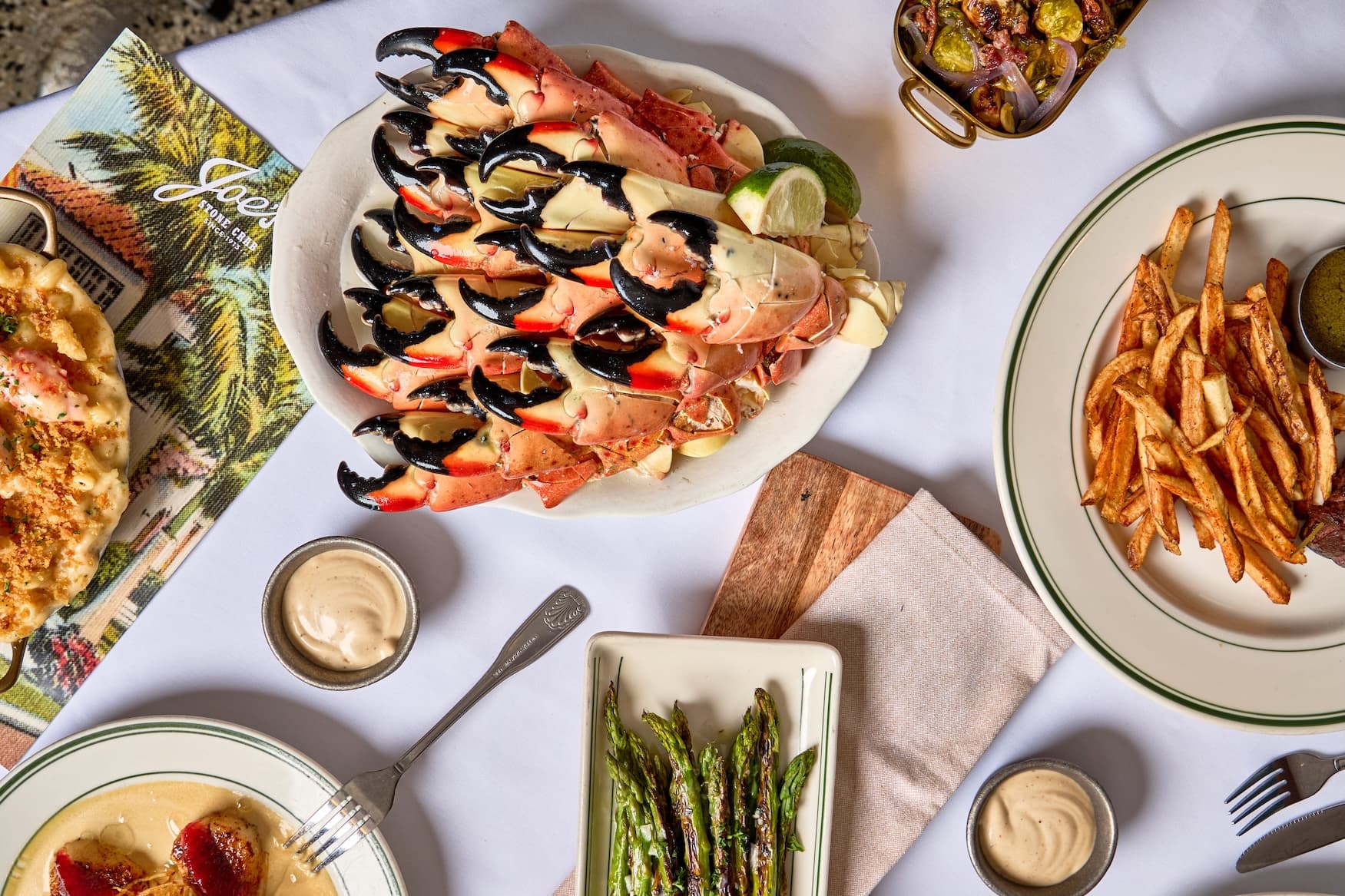 A platter of jumbo stone crab claws with mustard sauce, fries, mac and cheese, and grilled asparagus on a white tablecloth