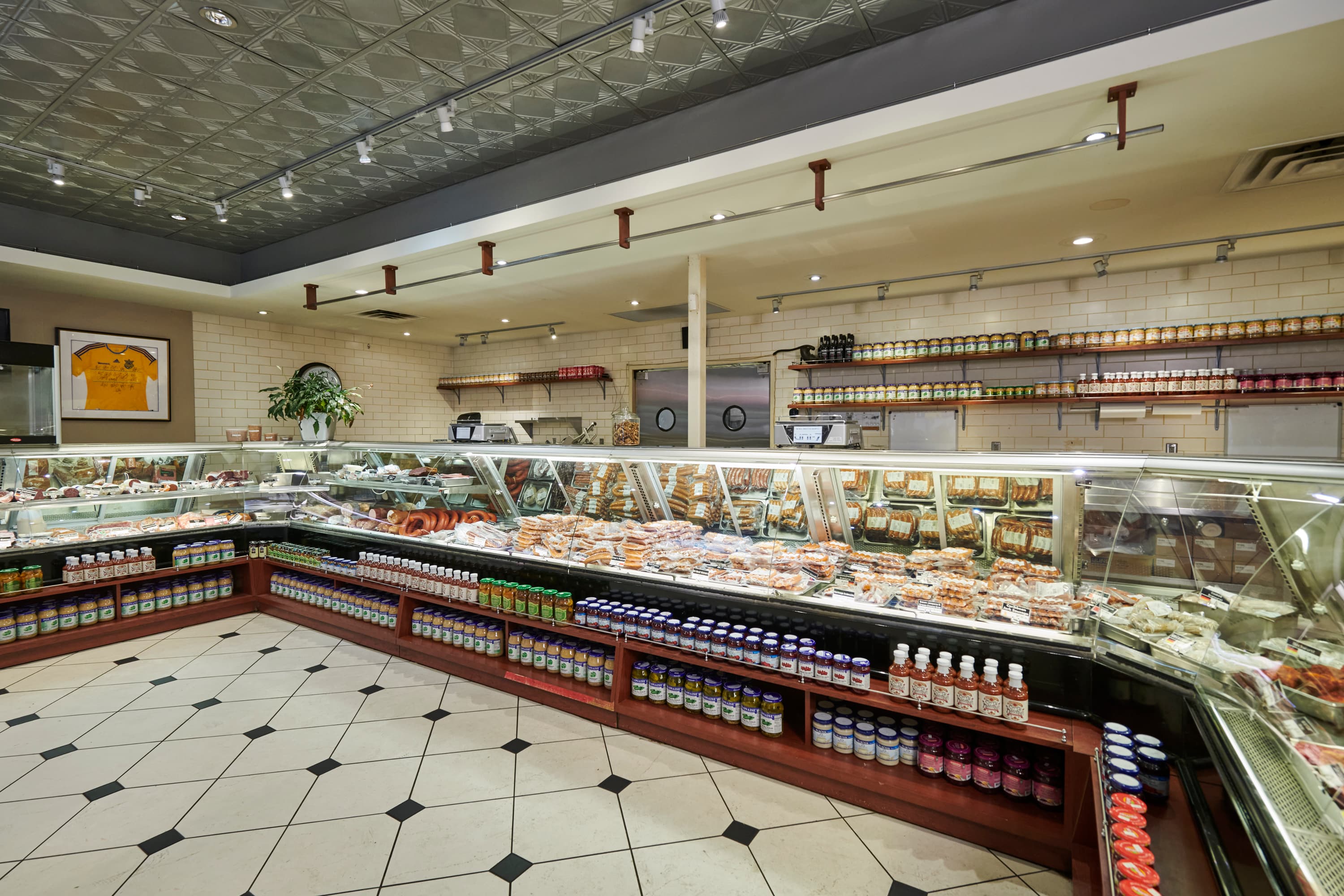 Kramarczuk's deli counter with rows of sausages, hams, and pickle jars under the display case, tiled floor and warm lighting