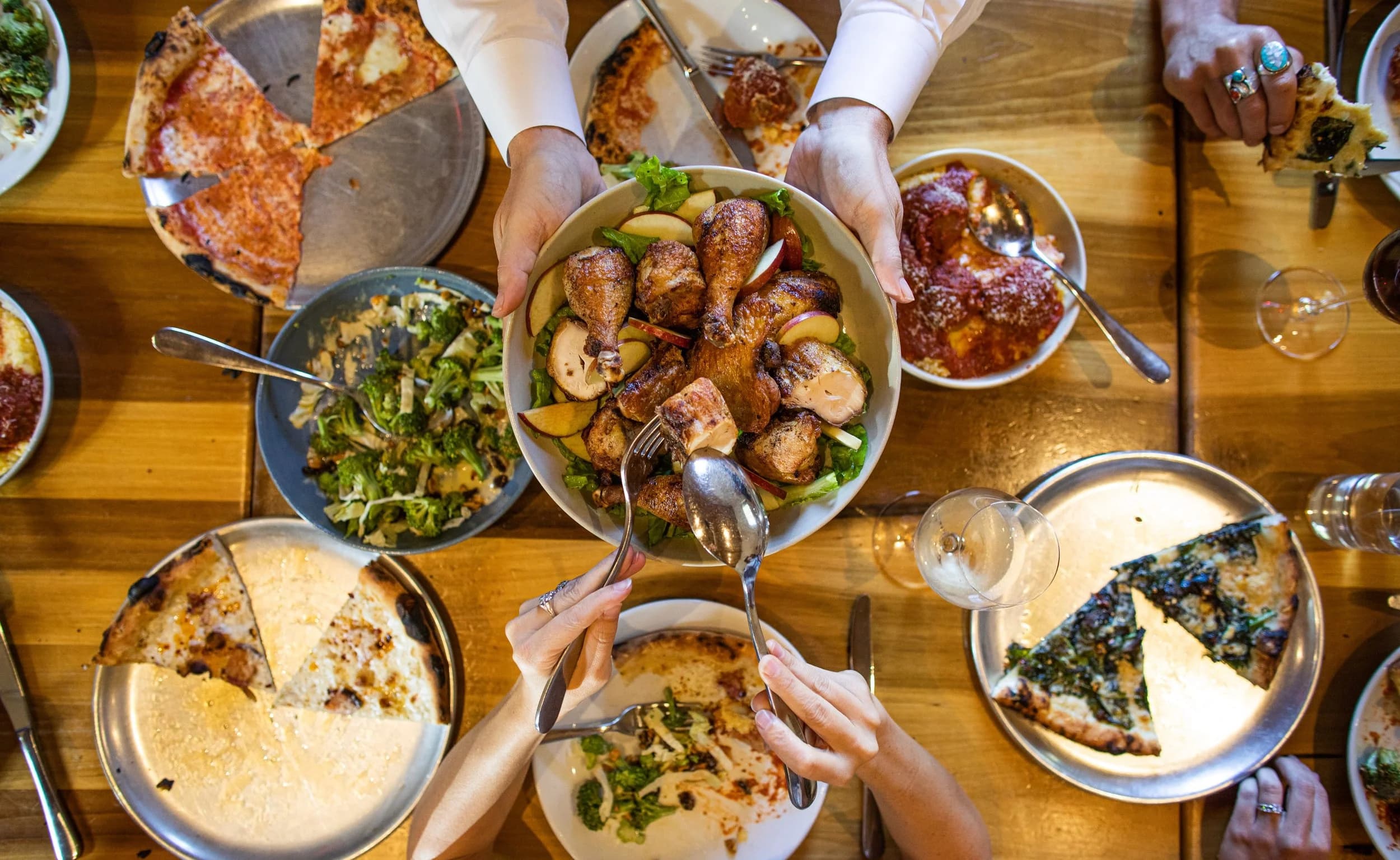 An overhead shot of a shared table at City House with wood-fired pizzas, roasted chicken, and salads