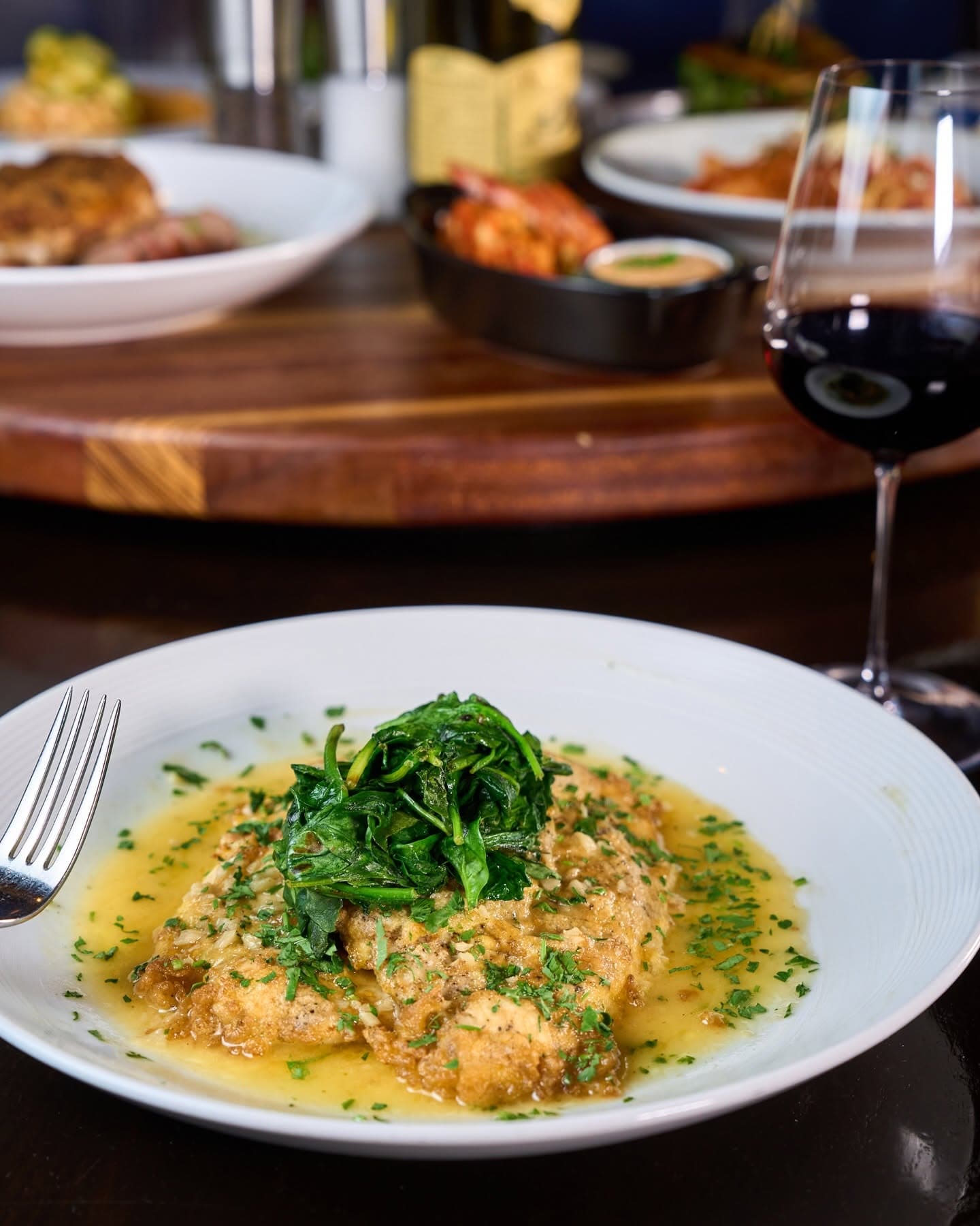 A breaded veal dish topped with sautéed greens beside a glass of red wine at Catherine Lombardi
