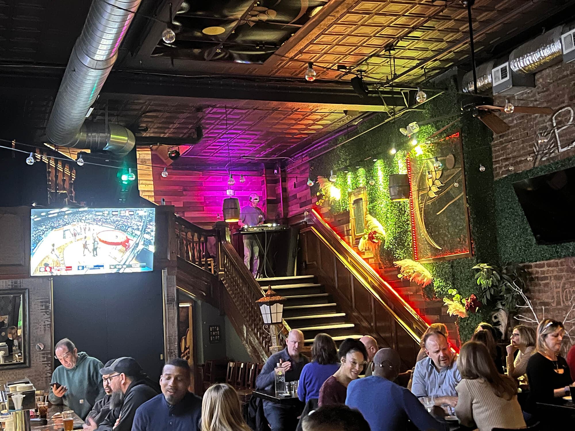 A packed bar with a DJ on the balcony above and colorful lighting inside Harvest Moon Brewery & Cafe