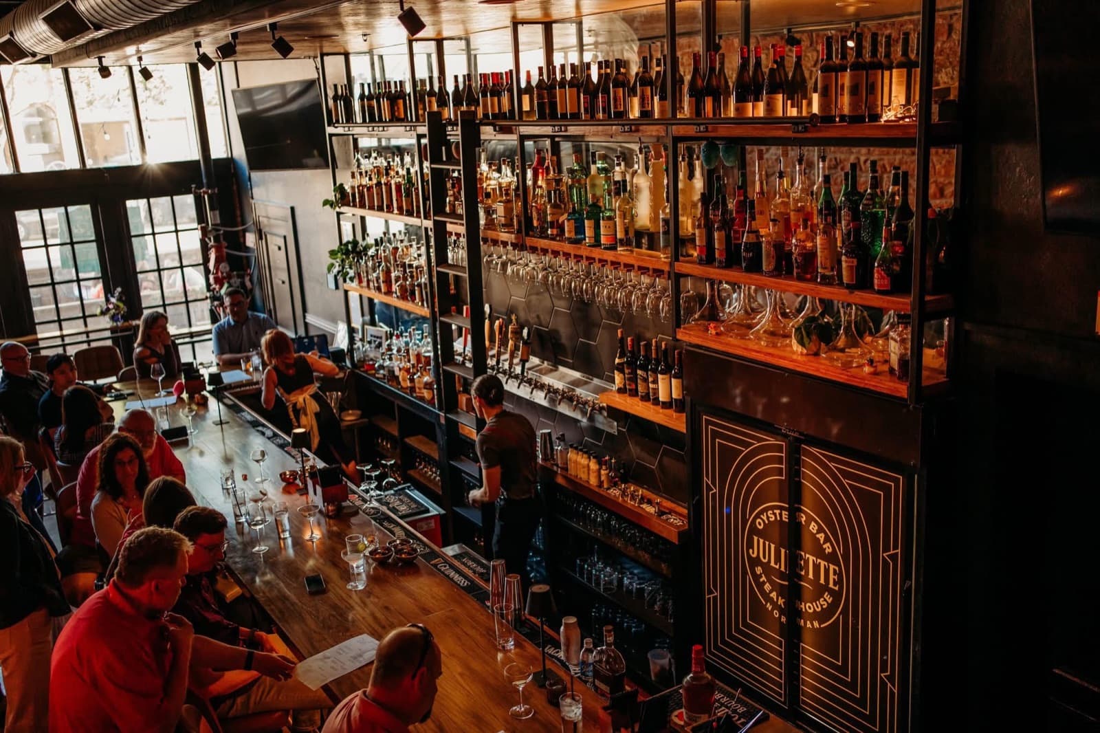 Juliette Oyster Bar & Steakhouse's back bar lined with bottles beneath its glowing sign, patrons seated at the counter