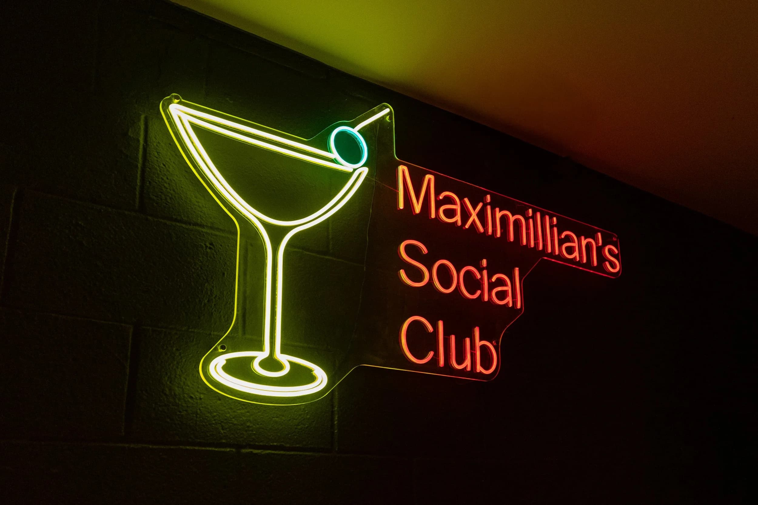 Maximillian's Social Club's martini-glass neon sign glowing on an exposed-brick wall