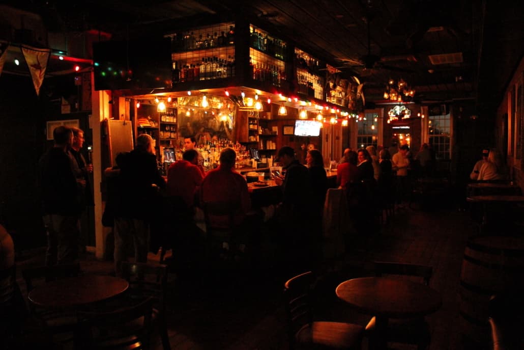 A dimly lit bar scene at City Grocery with people gathered at the bar under string lights and an antique-lined back bar