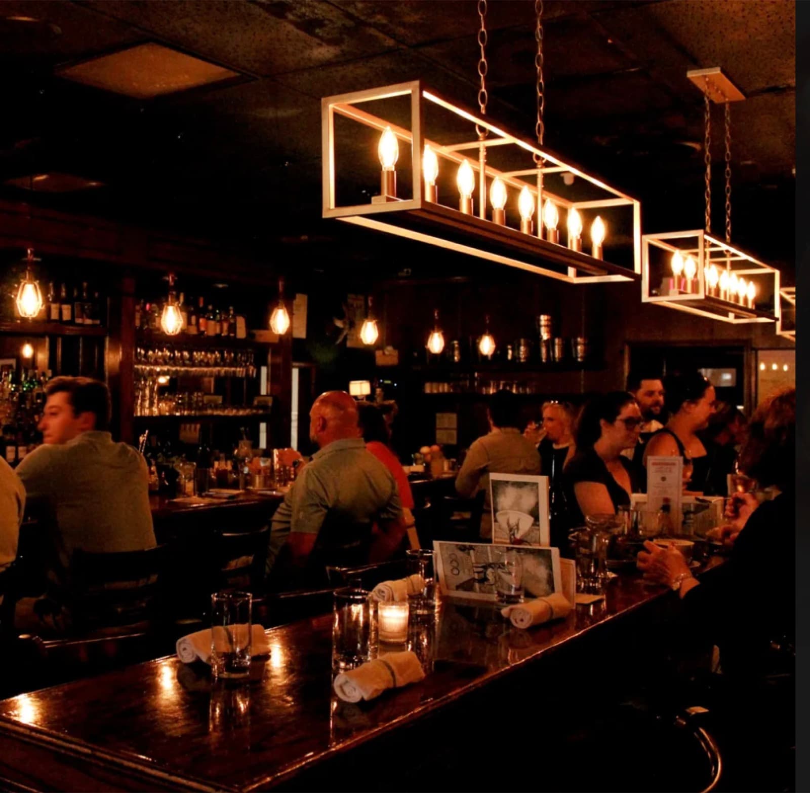 Snackbar's dim dining room with box-frame pendant lights and patrons seated along the bar