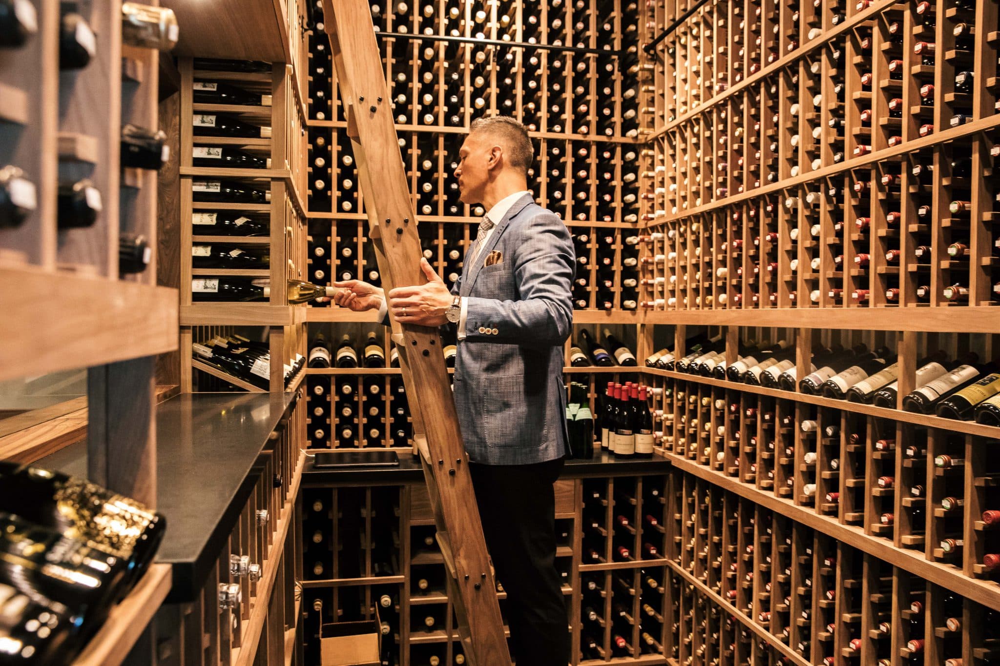 A sommelier in a blazer selecting a bottle from Protégé's floor-to-ceiling wine cellar racks