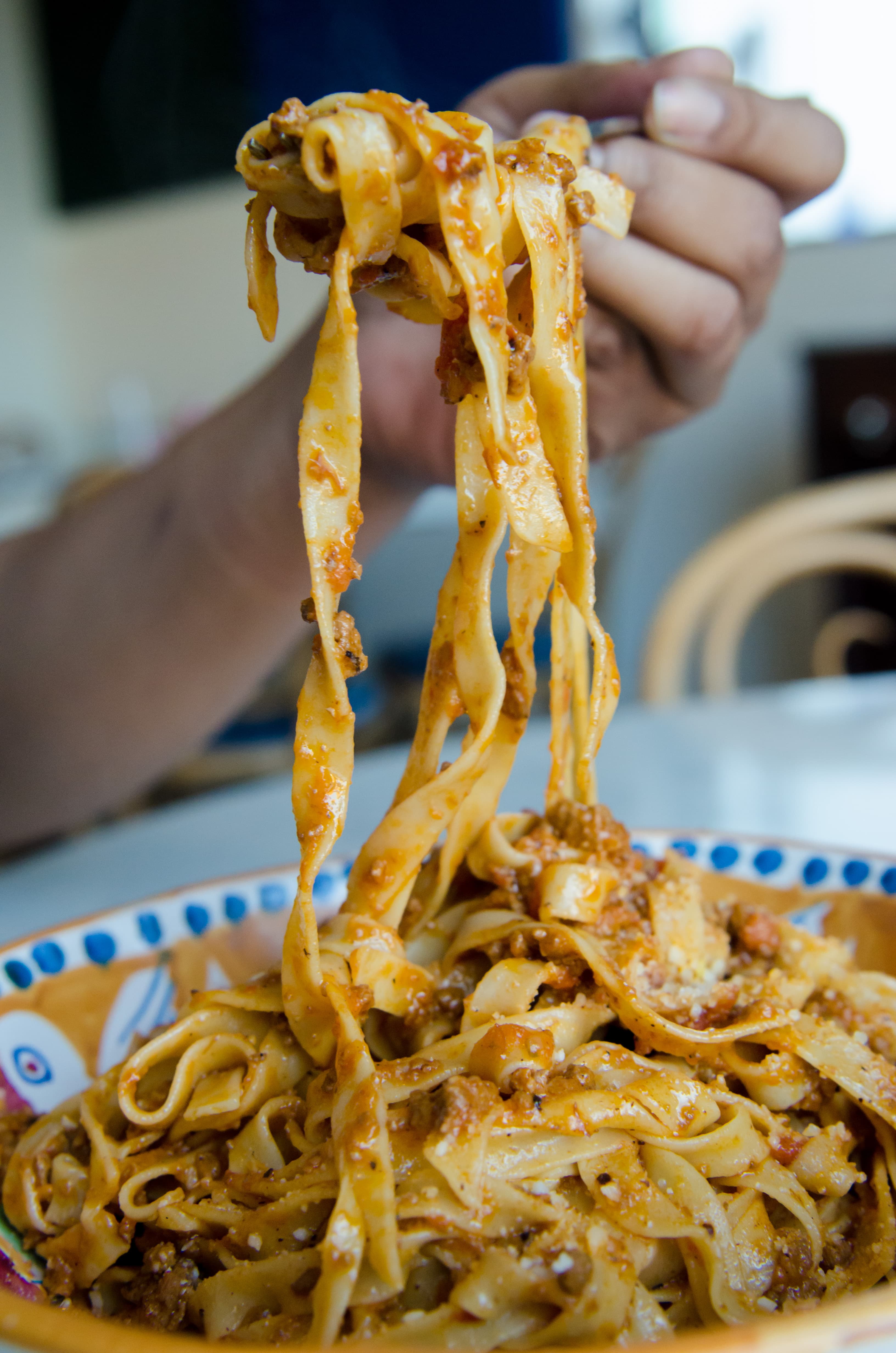 A hand lifting a forkful of house-made tagliatelle with meat ragu from a full bowl at DiAnoia's Eatery