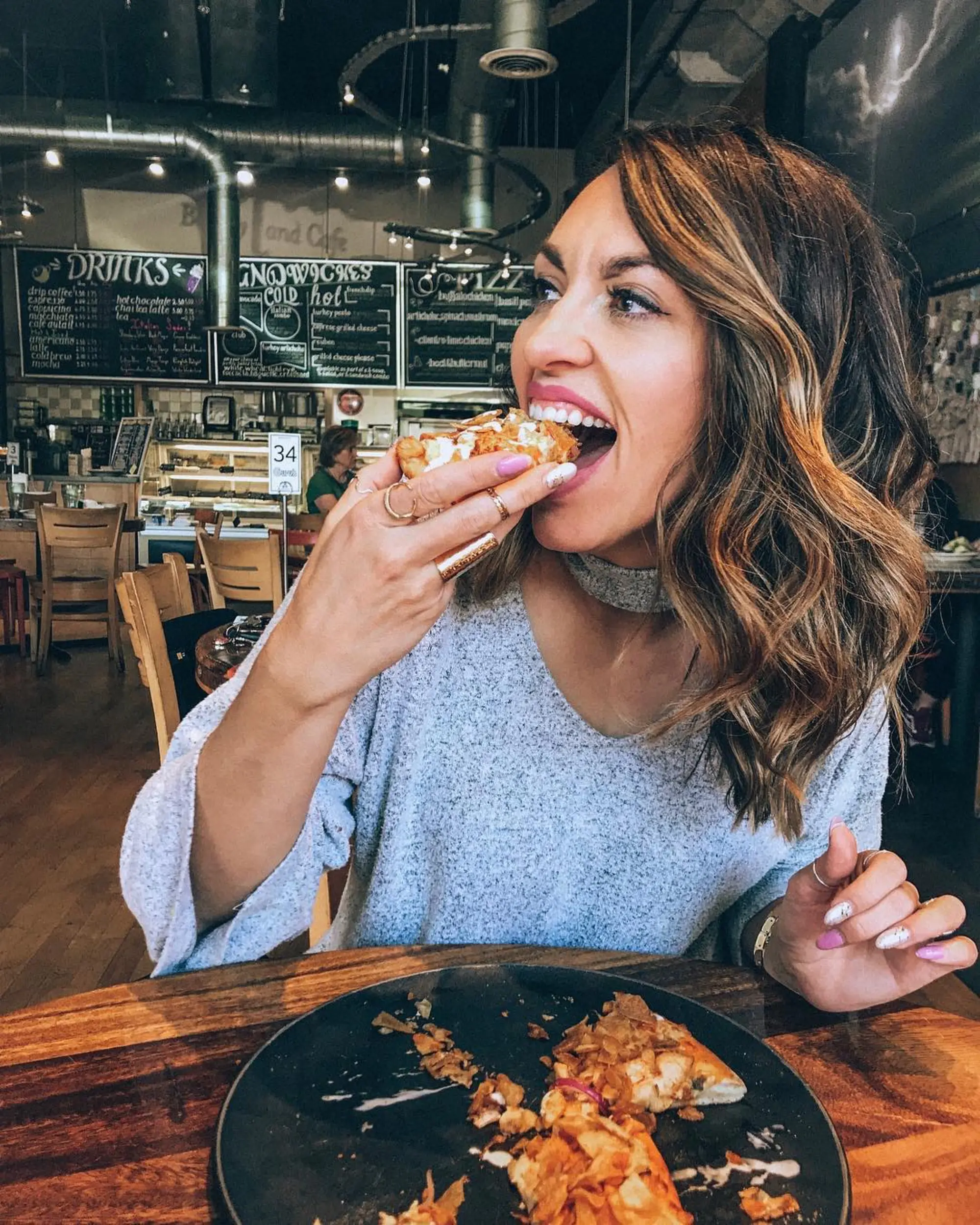A woman biting into a loaded naan wrap in front of Guru's Cafe's chalkboard drinks and sandwiches menu