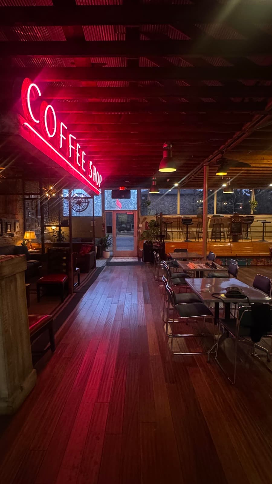 Rugged Grounds' red neon 'Coffee Shop' sign glowing above the wood-floored seating area