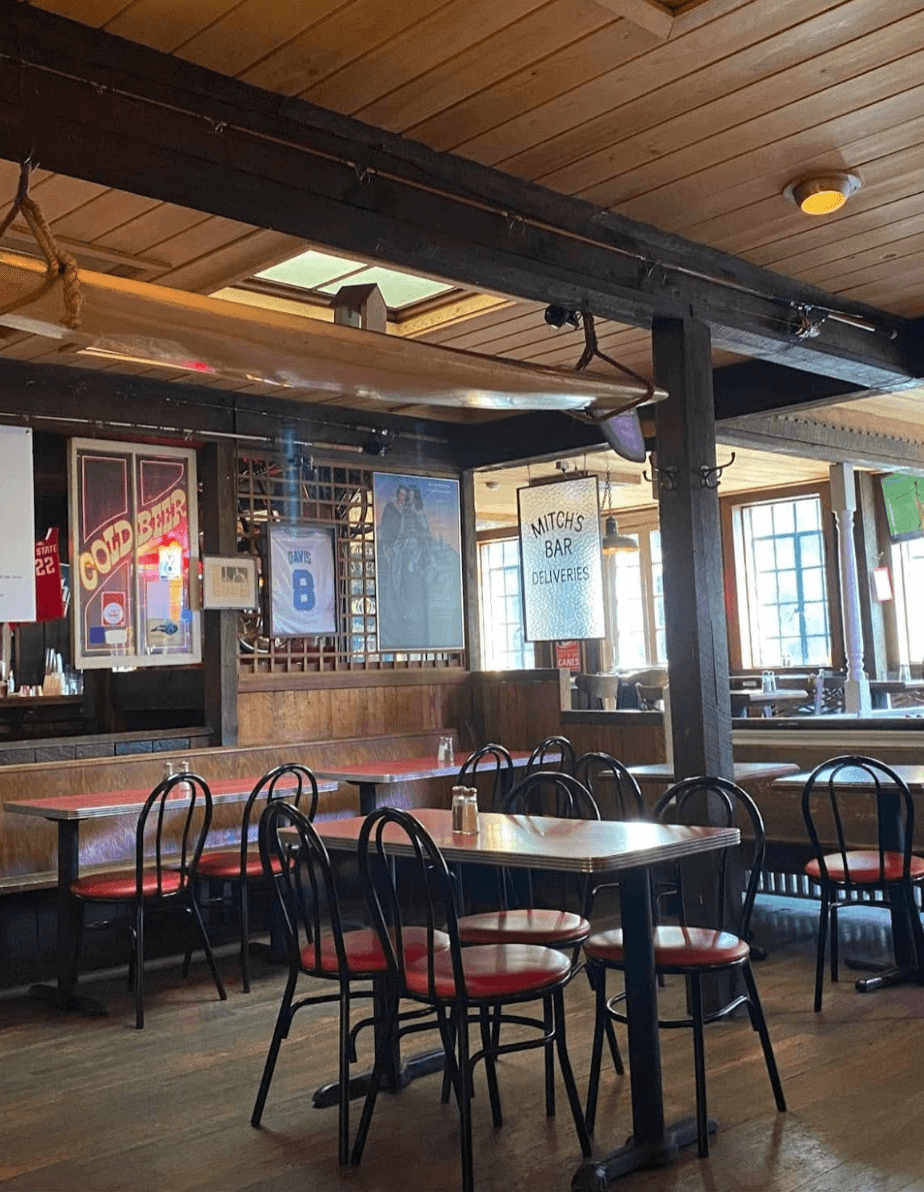 Mitch's Tavern's wood-paneled dining room with red vinyl booth seating, vintage signage, and a canoe hung from the ceiling