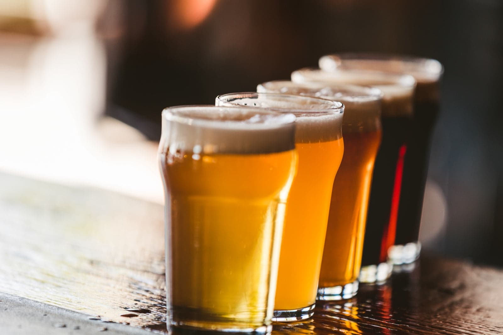 A lineup of five beers in pint glasses, ranging from pale gold to dark stout, on a wooden bar at Fisher Brewing Company