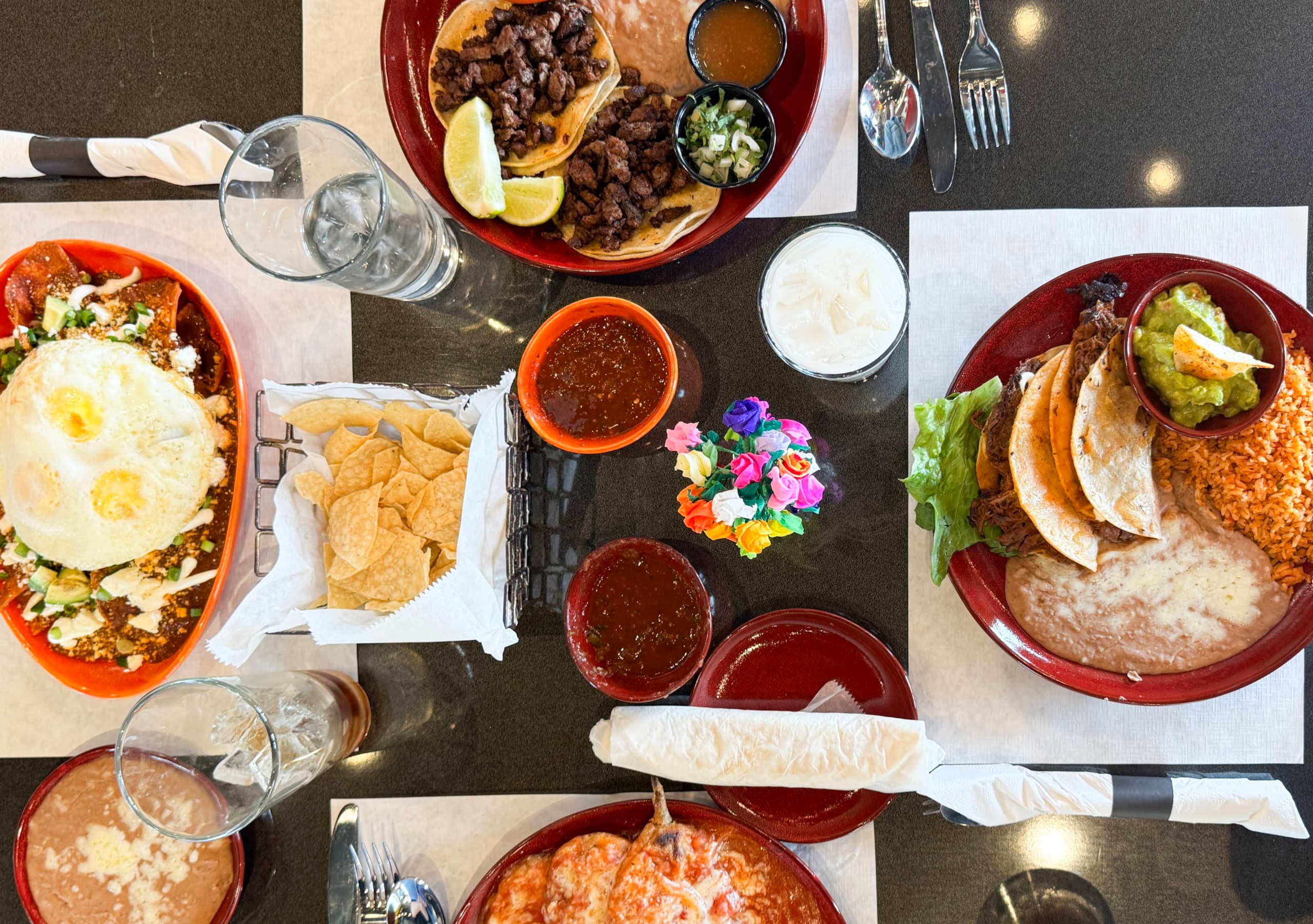 An overhead spread of Red Iguana's Mexican plates — steak tacos, huevos rancheros with mole, shredded beef tacos with guacamole, and chips with salsa