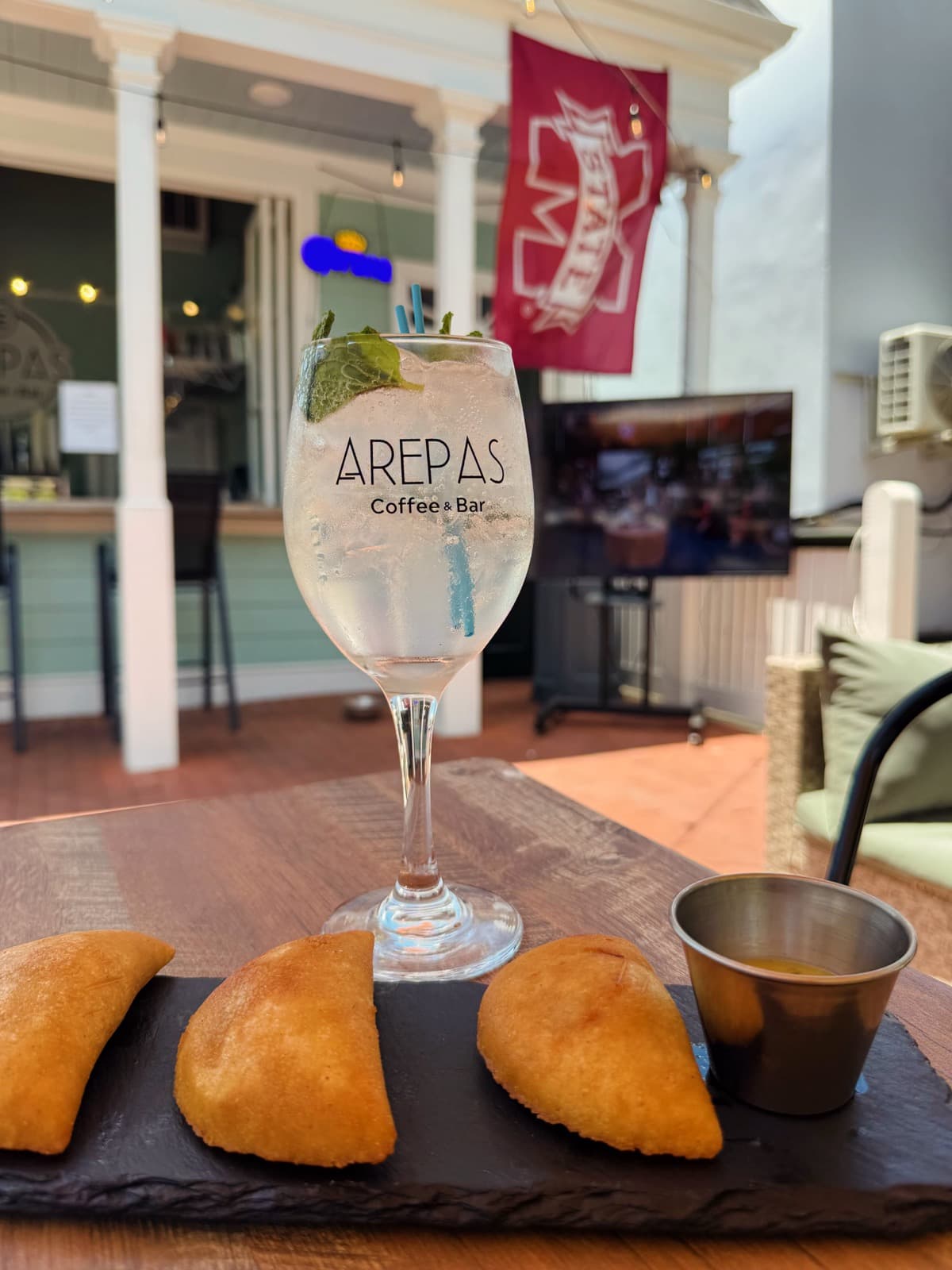 Three empanadas beside a branded Arepas Coffee & Bar wine glass, an MSU flag in the background