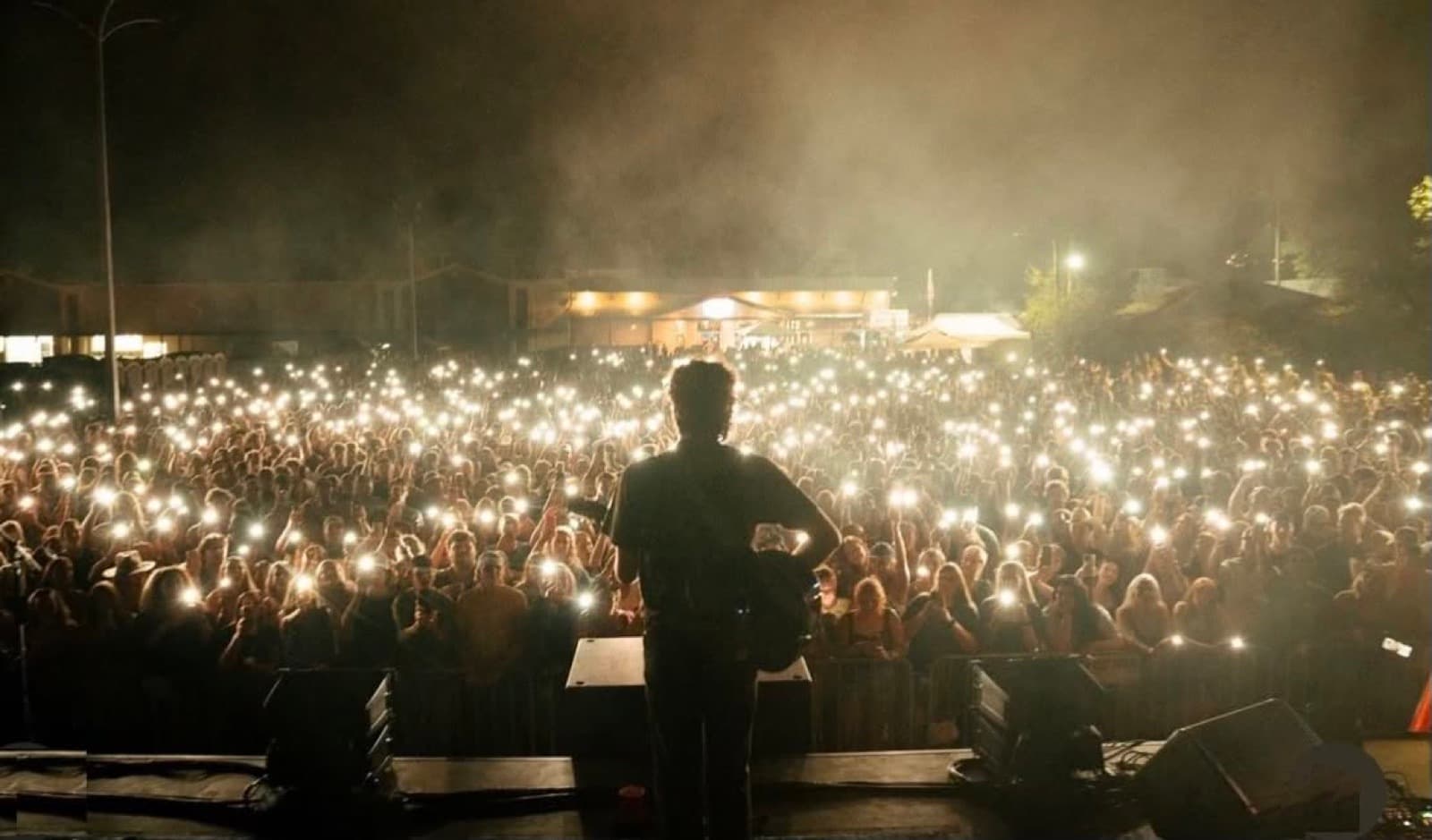 A packed outdoor crowd at Rick's Cafe holding up phone lights toward a performer on stage