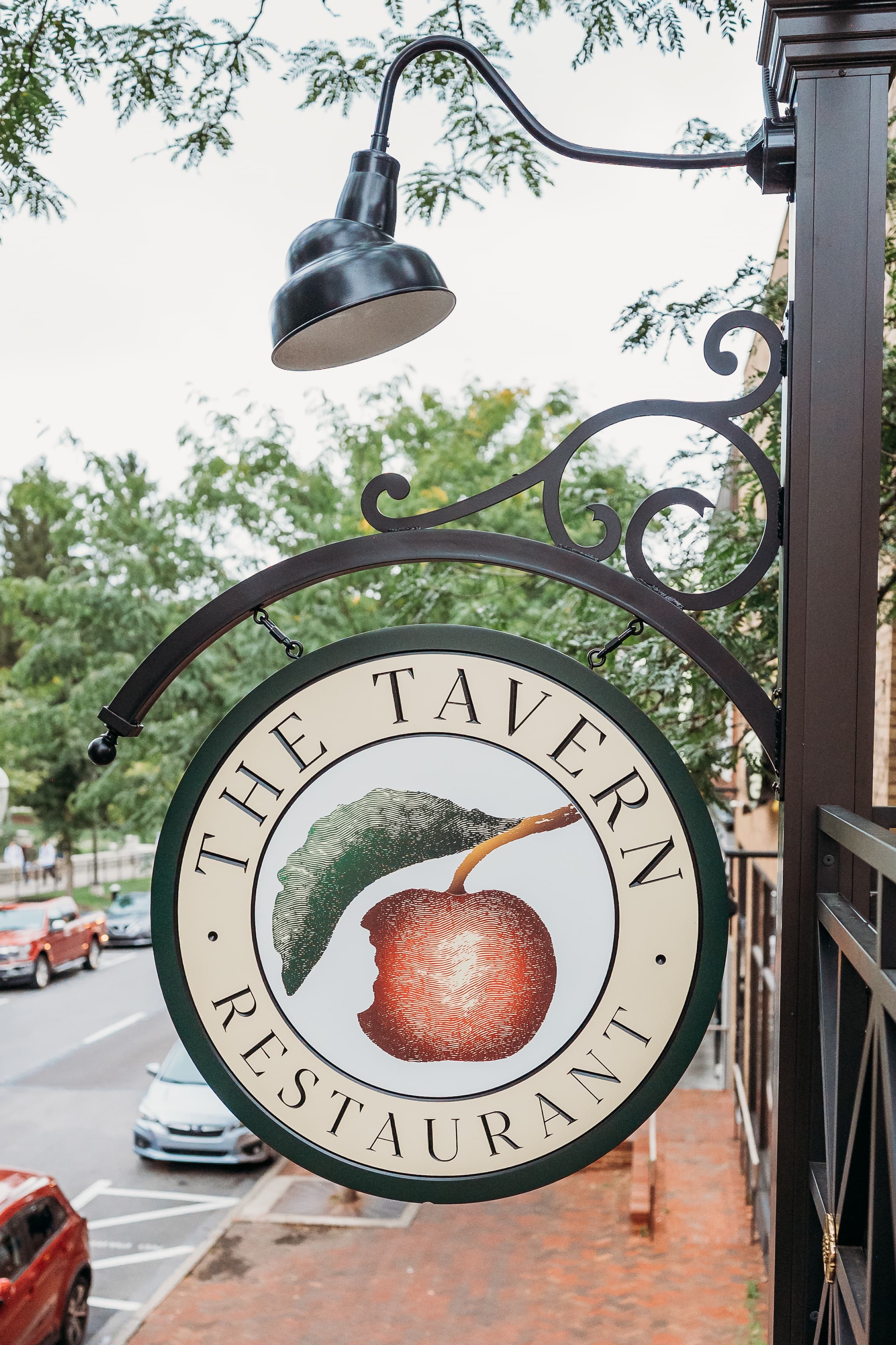 The hanging street sign for The Tavern Restaurant, with an apple-and-leaf emblem, above a downtown State College sidewalk