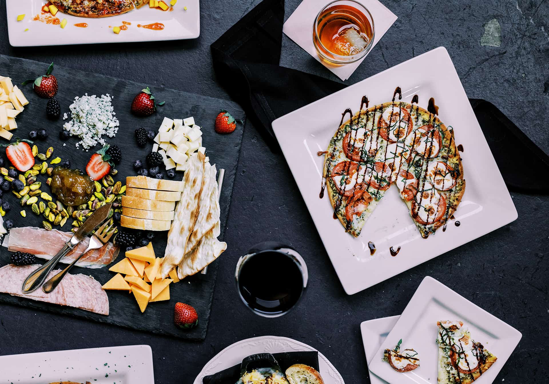 A charcuterie board, a margherita flatbread and glasses of wine spread across a table at Zannotti's Wine Bar