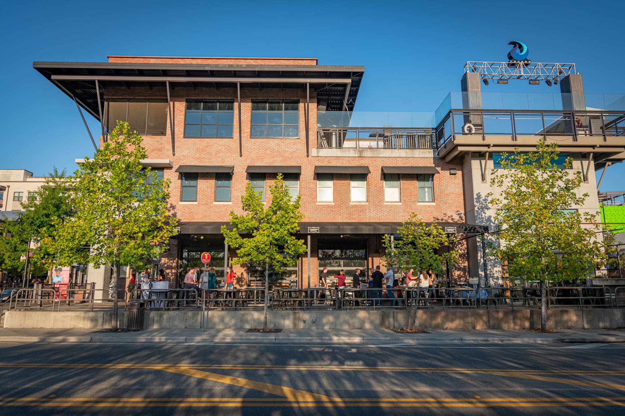 Madison Social's brick building exterior with a rooftop deck, string of patio tables, and diners on the sidewalk