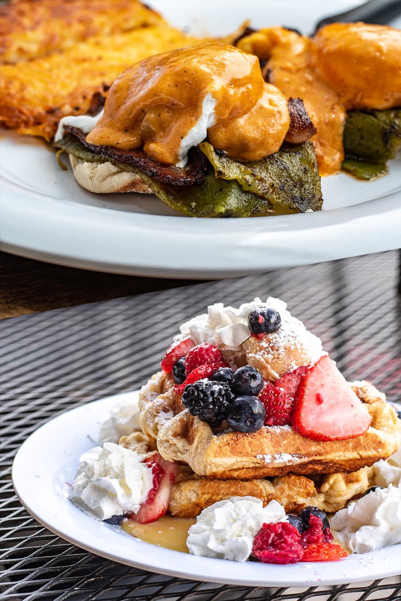 Two poached eggs over hashbrowns and corned beef, plus a stack of berry-topped Belgian waffles, on Baja Café's outdoor patio table