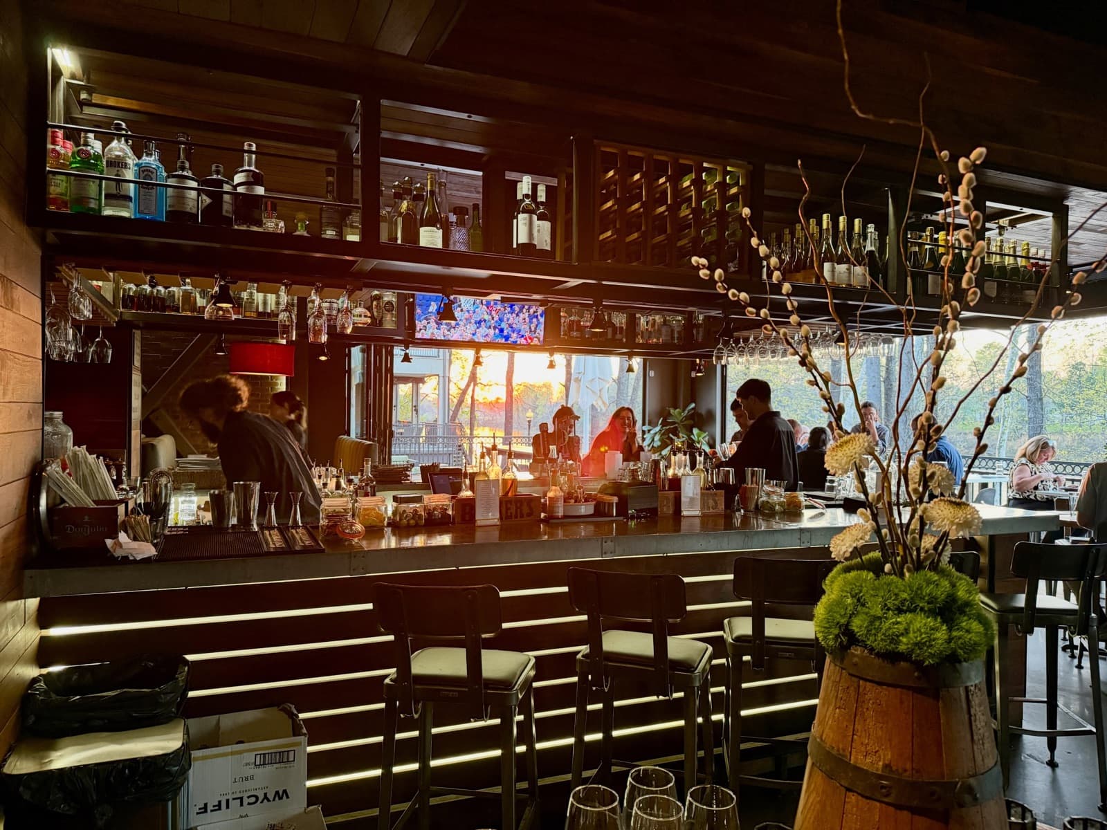 River's bar at sunset, bartenders working the counter with the Black Warrior riverfront glowing through the windows
