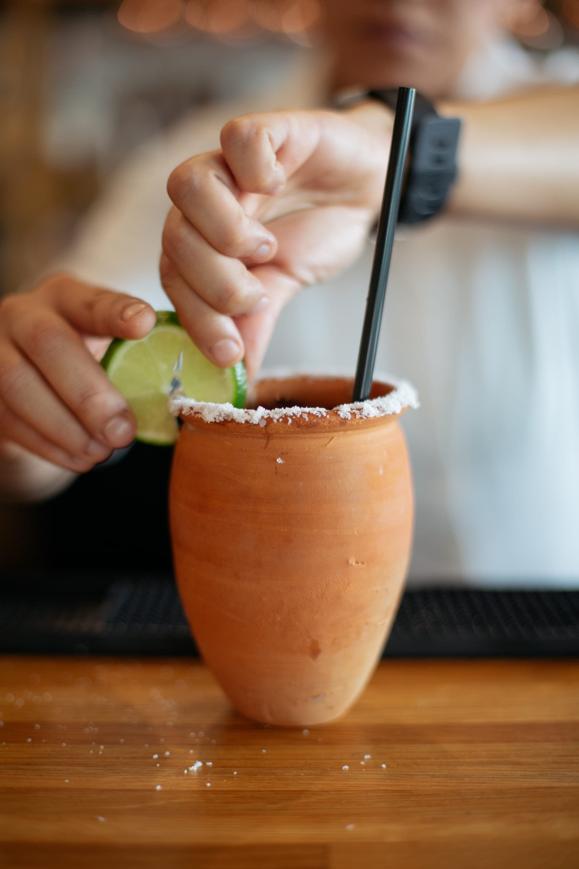 A bartender salting the rim of a terracotta cup and adding a lime wedge to a margarita at Milo All Day